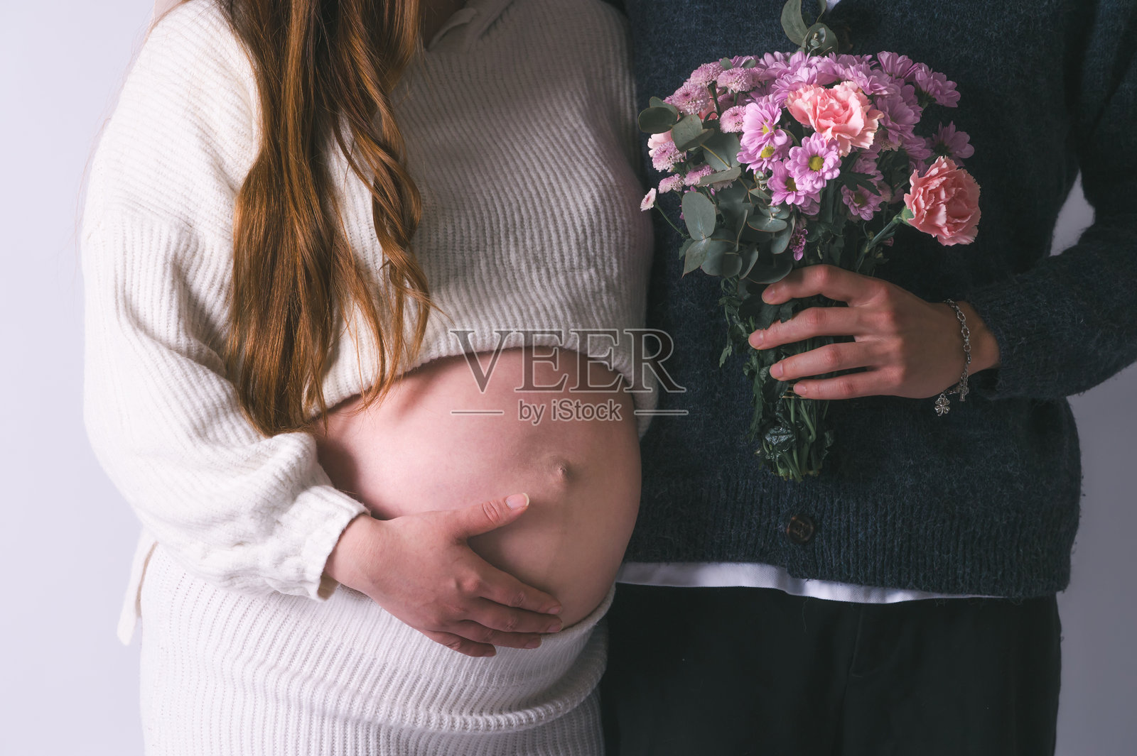 孕妇夫妇近距离接触,手握花朵,双手放在孕肚上,未来母亲和父亲的手紧握着大肚子。照片摄影图片