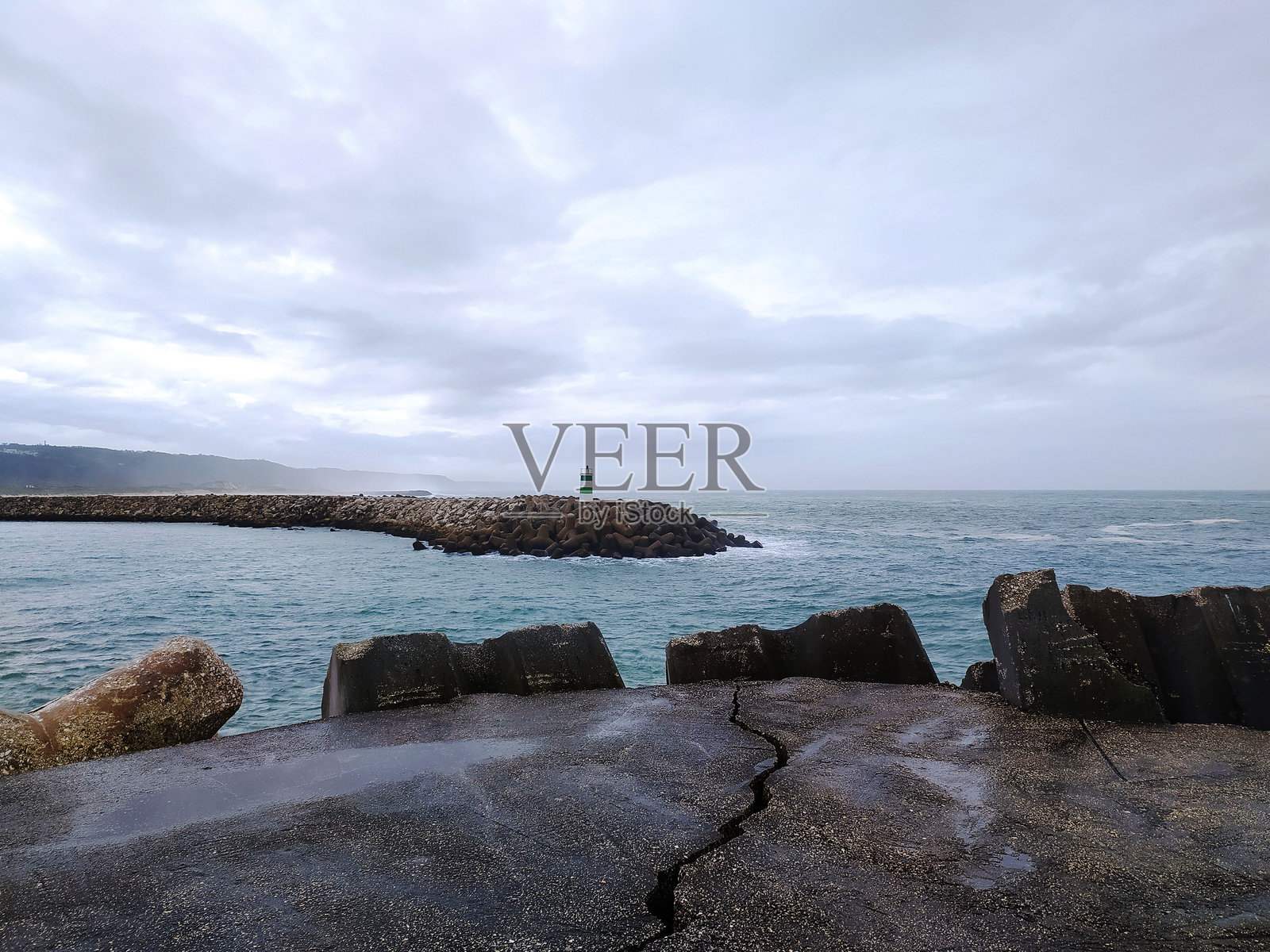 阴郁的海景,前景是通向远处灯塔的防波堤。混凝土结构勾勒出画面,增添了深度。非常适合表现韧性和引导的主题。照片摄影图片