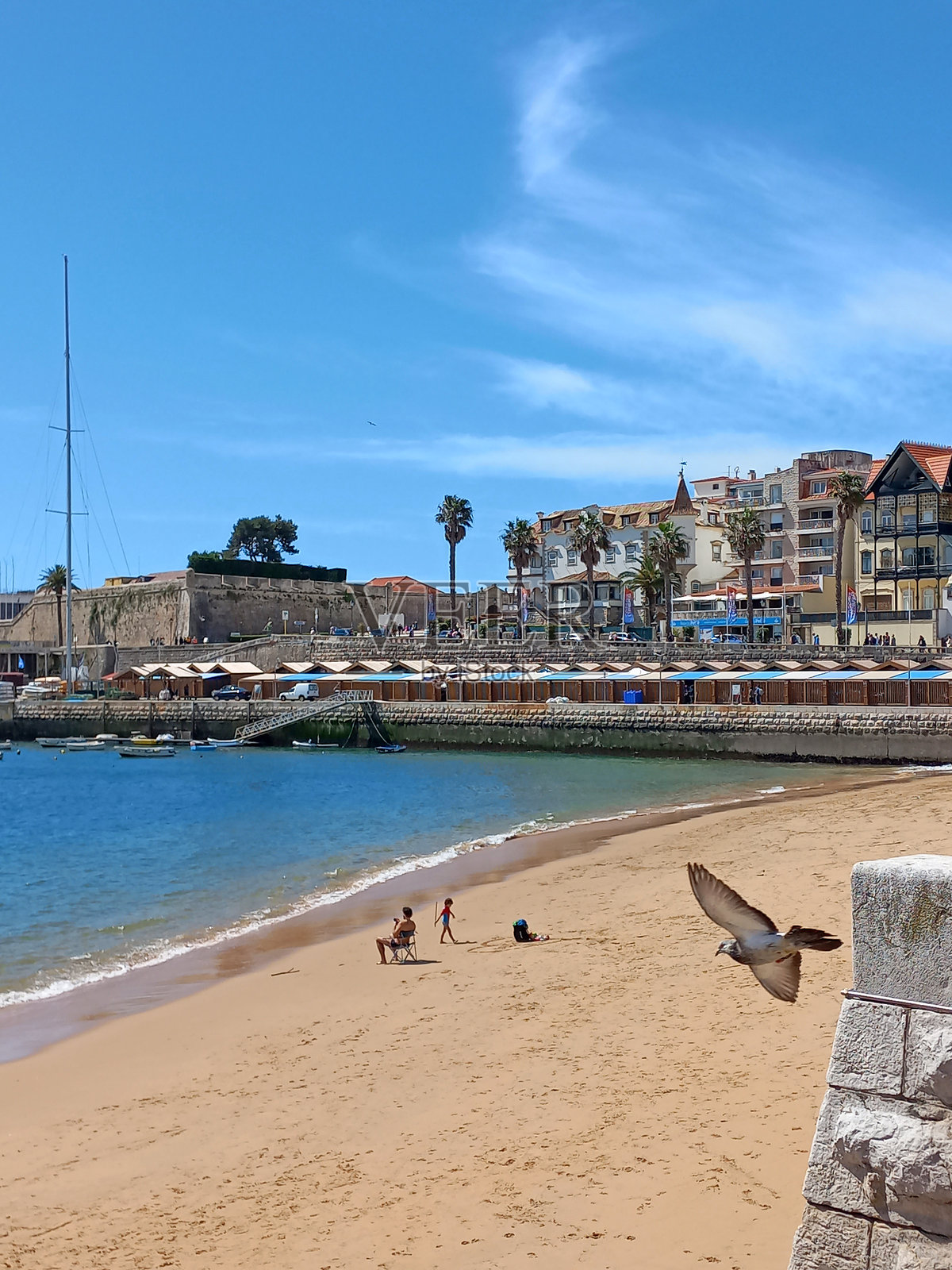 家庭在葡萄牙卡斯凯什海滩享受阳光明媚的一天,背景是宁静的海水和历史建筑。照片摄影图片