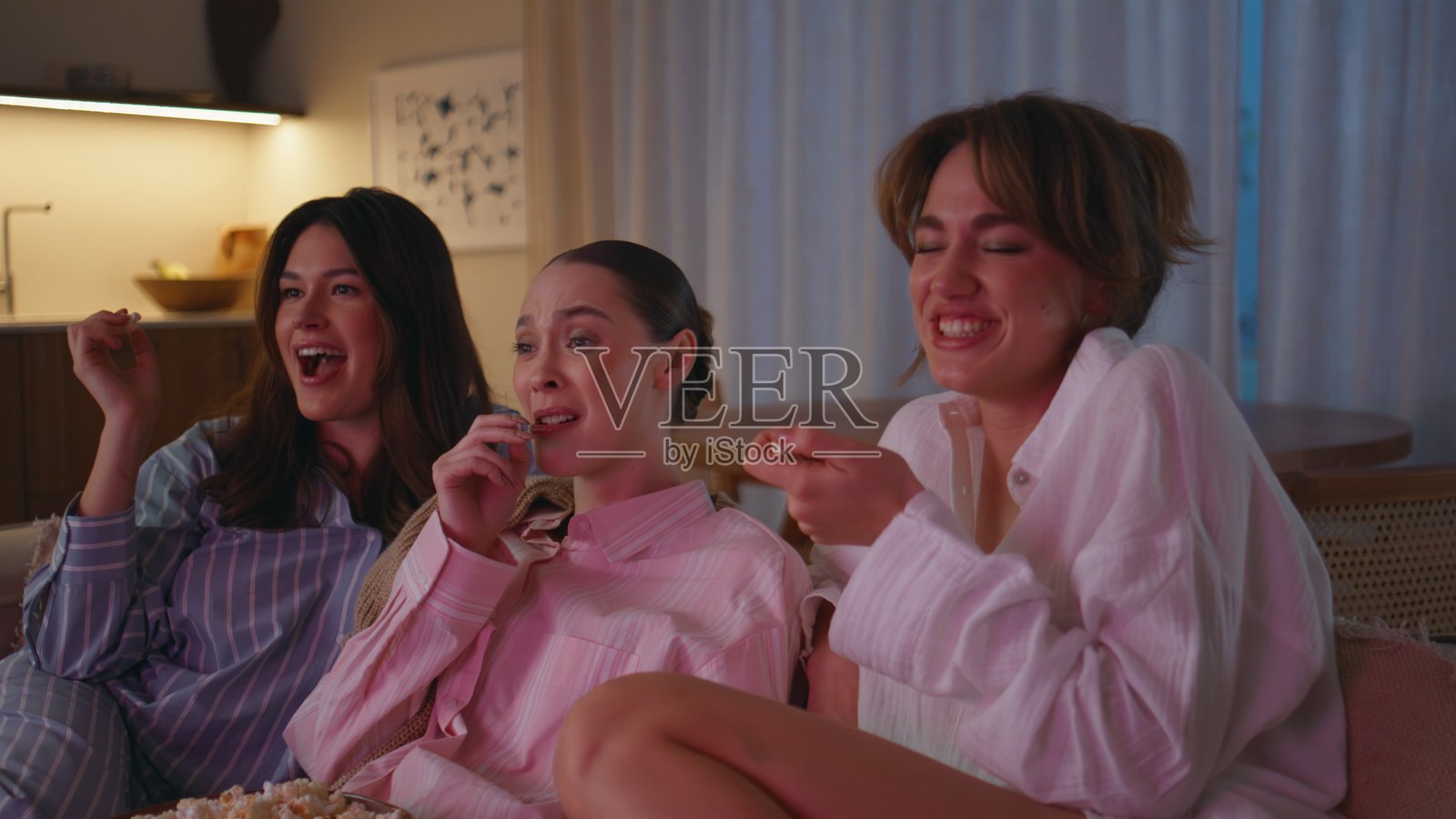 穿着睡衣的女性在沙发上观看喜剧节目,开心地大笑,特写镜头。照片摄影图片