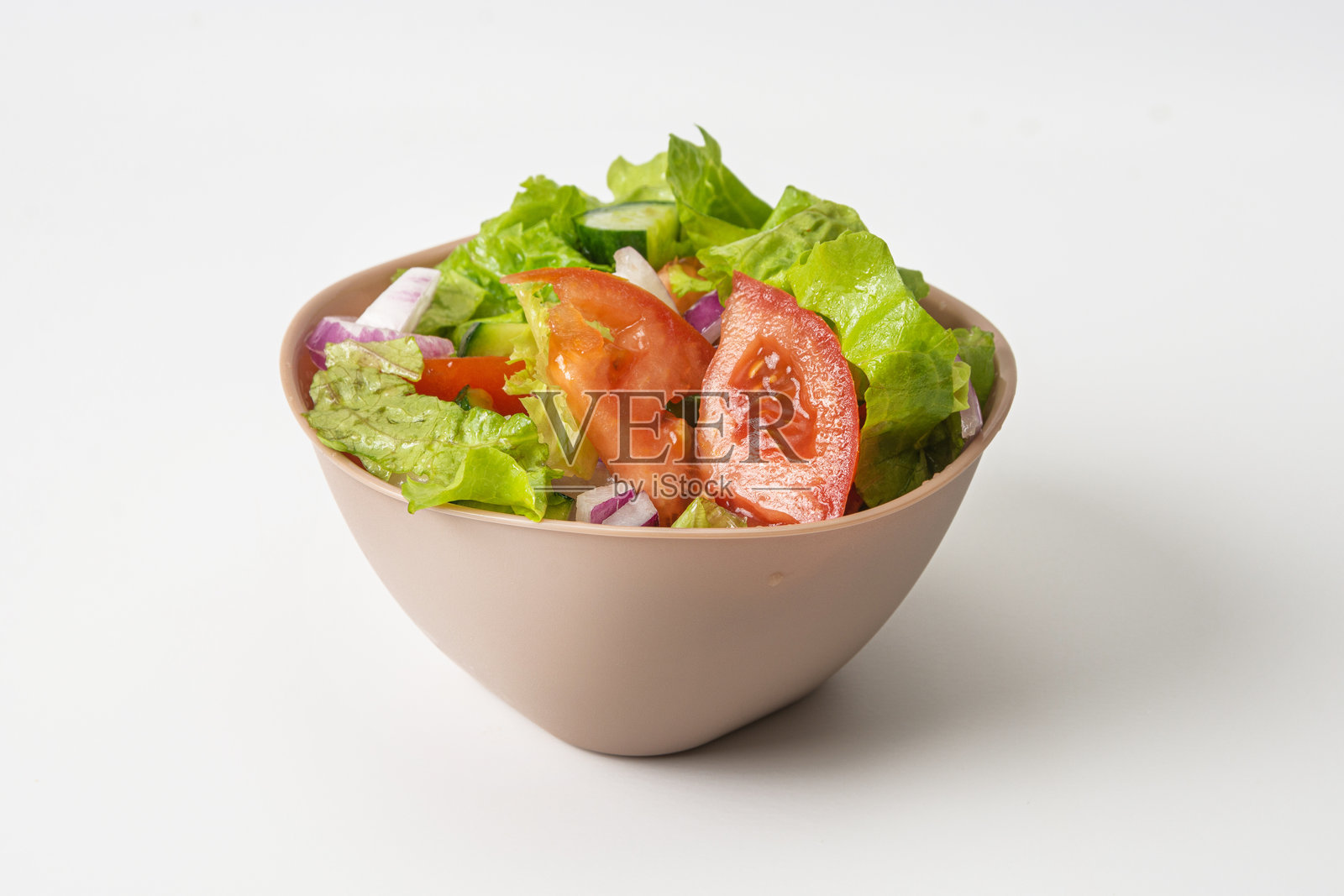 素食沙拉,配有黄瓜、西红柿和红洋葱。素食沙拉放在米色深盘中,背景为白色。照片摄影图片