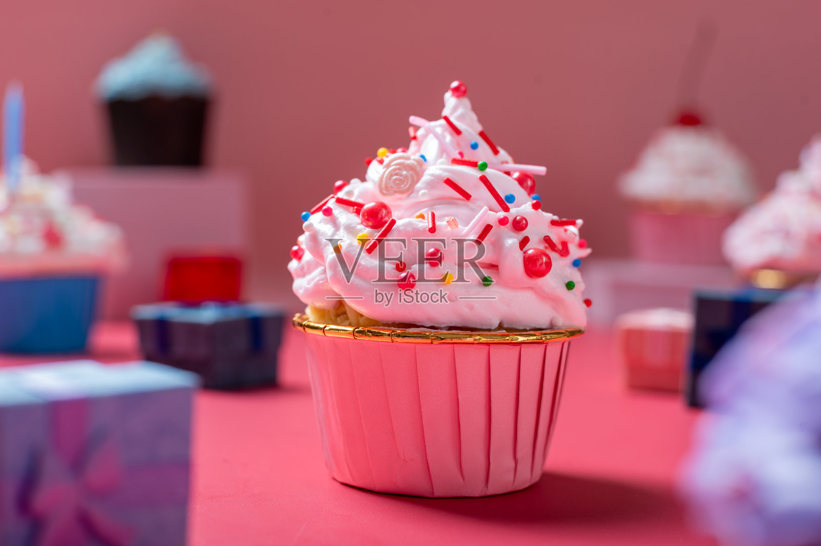 一个粉色的杯子蛋糕,上面装饰着蓬松的白色糖霜、红色糖屑和装饰性糖果珍珠,背景是相配的粉色。照片摄影图片