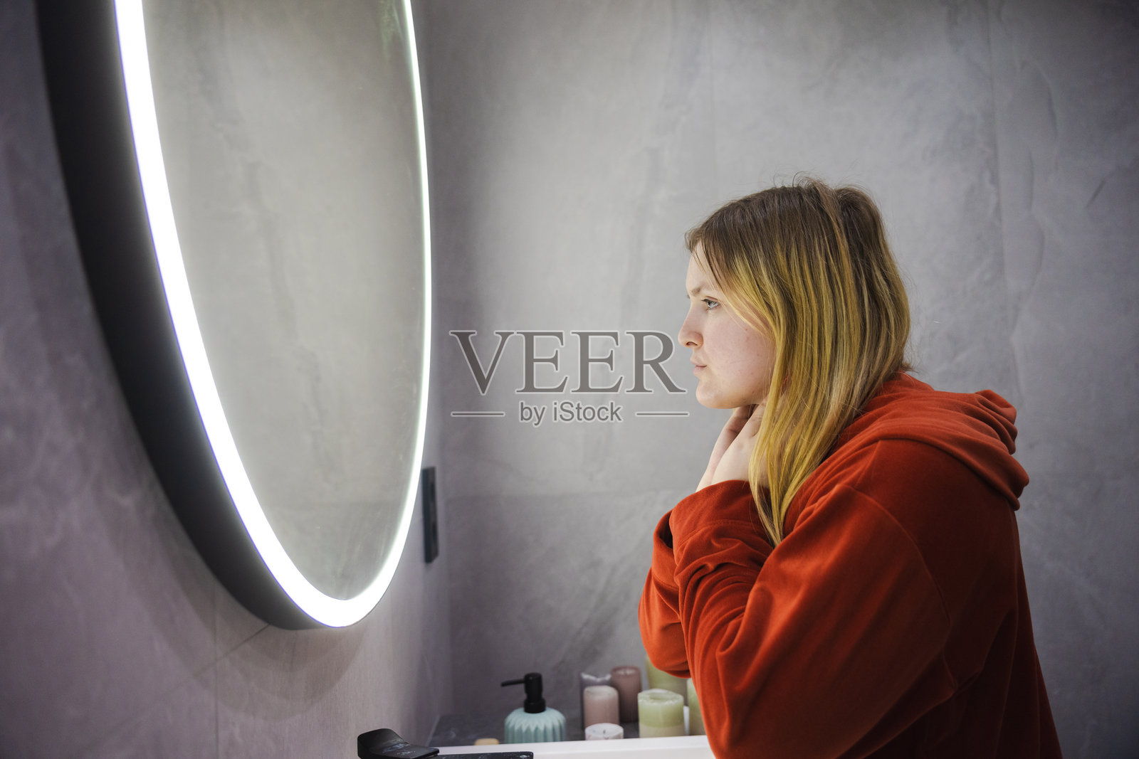 年轻女子穿着红色长袍,凝视着自己在发光圆形镜子中的倒影,脸颊靠在手上,神情沉思。照片摄影图片