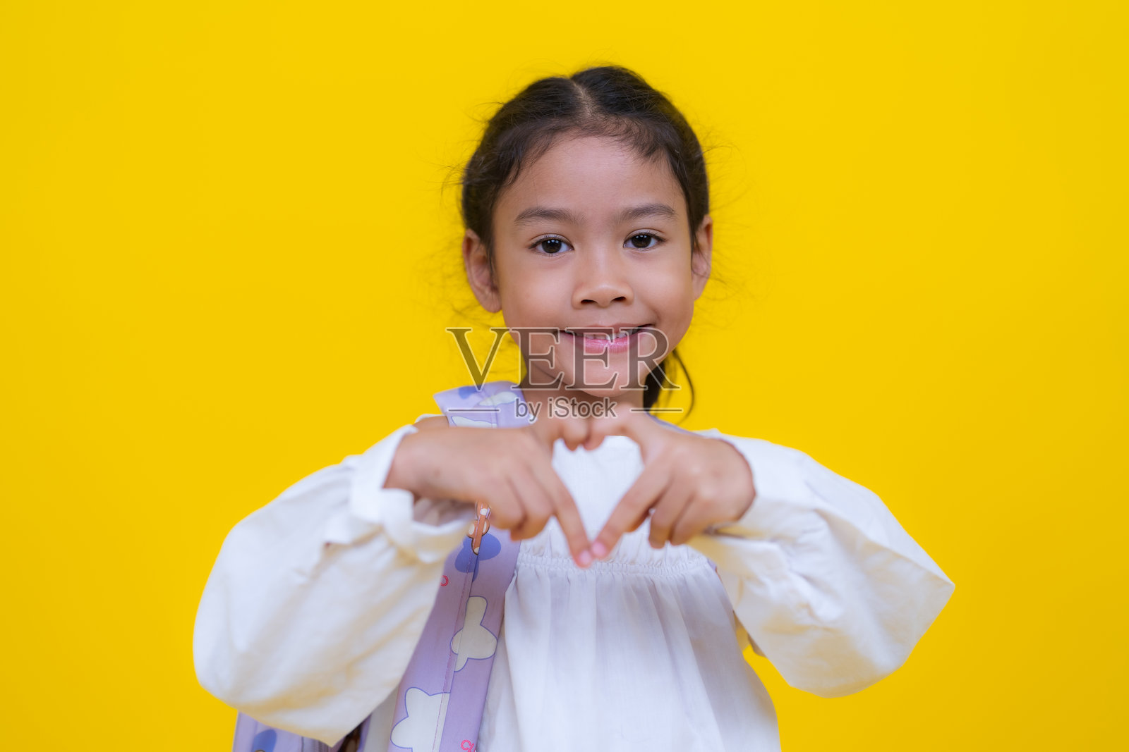 微笑的学生在黄色背景下用手做出心形手势照片摄影图片