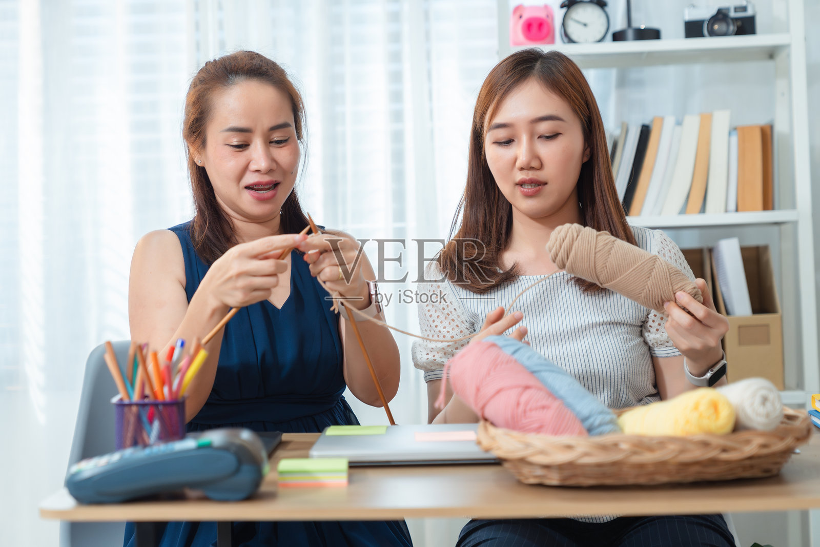 两位亚洲女性在家中一起坐着练习编织,享受友谊、创造力和轻松的手工艺时光。照片摄影图片