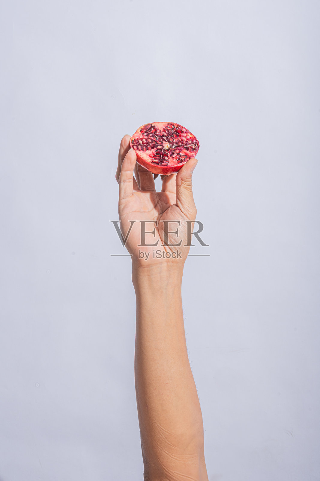 一只手握着半个石榴,展示出鲜艳的红色种子和分段的图案,背景为简单的浅灰色,构图干净简约。照片摄影图片