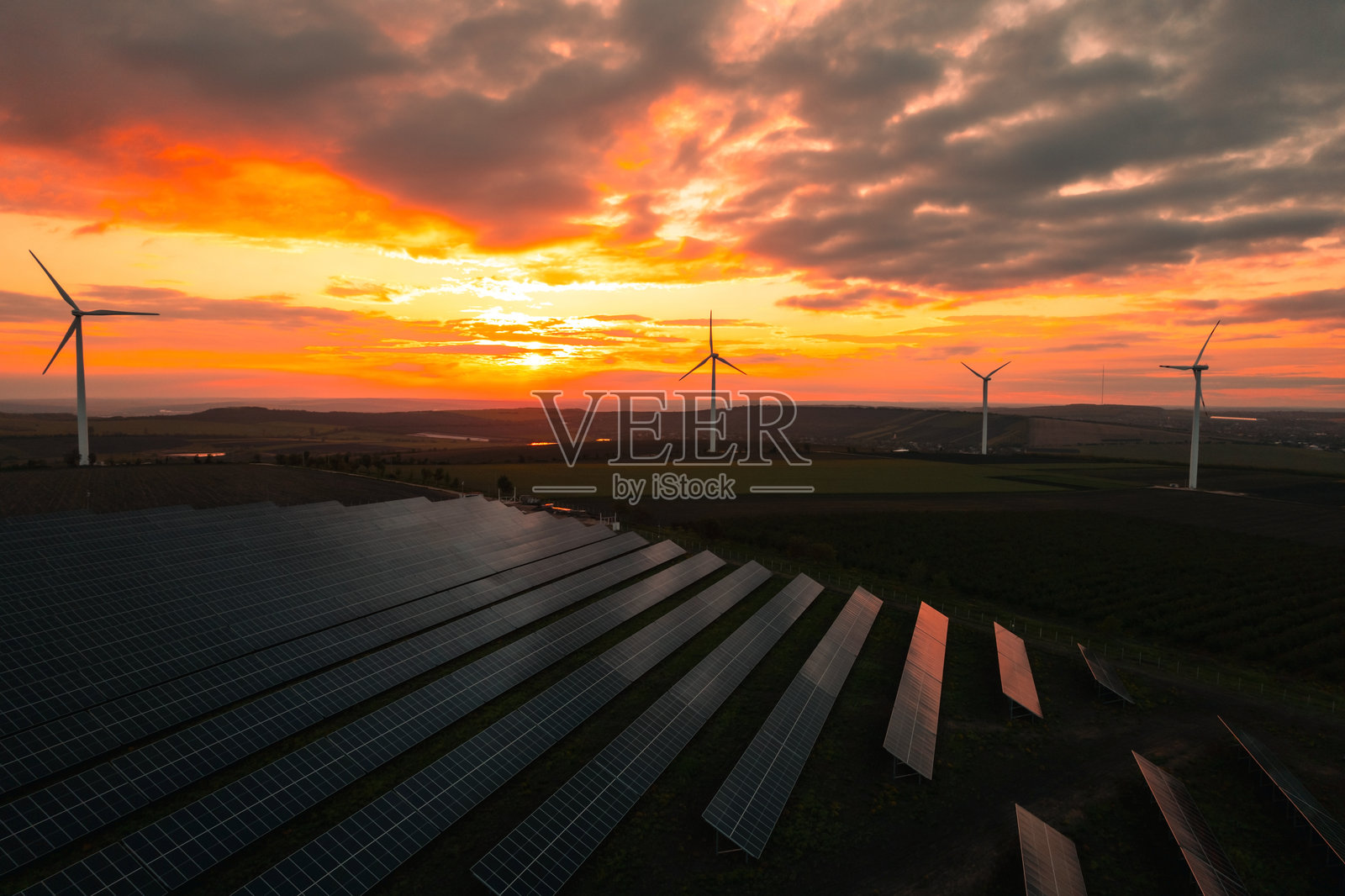 风力发电机公园的鸟瞰图,产生绿色能源电力。日落时分的太阳能电池板公园和风力涡轮机。绿色能源减少碳排放,使地球更清洁、更生态。照片摄影图片