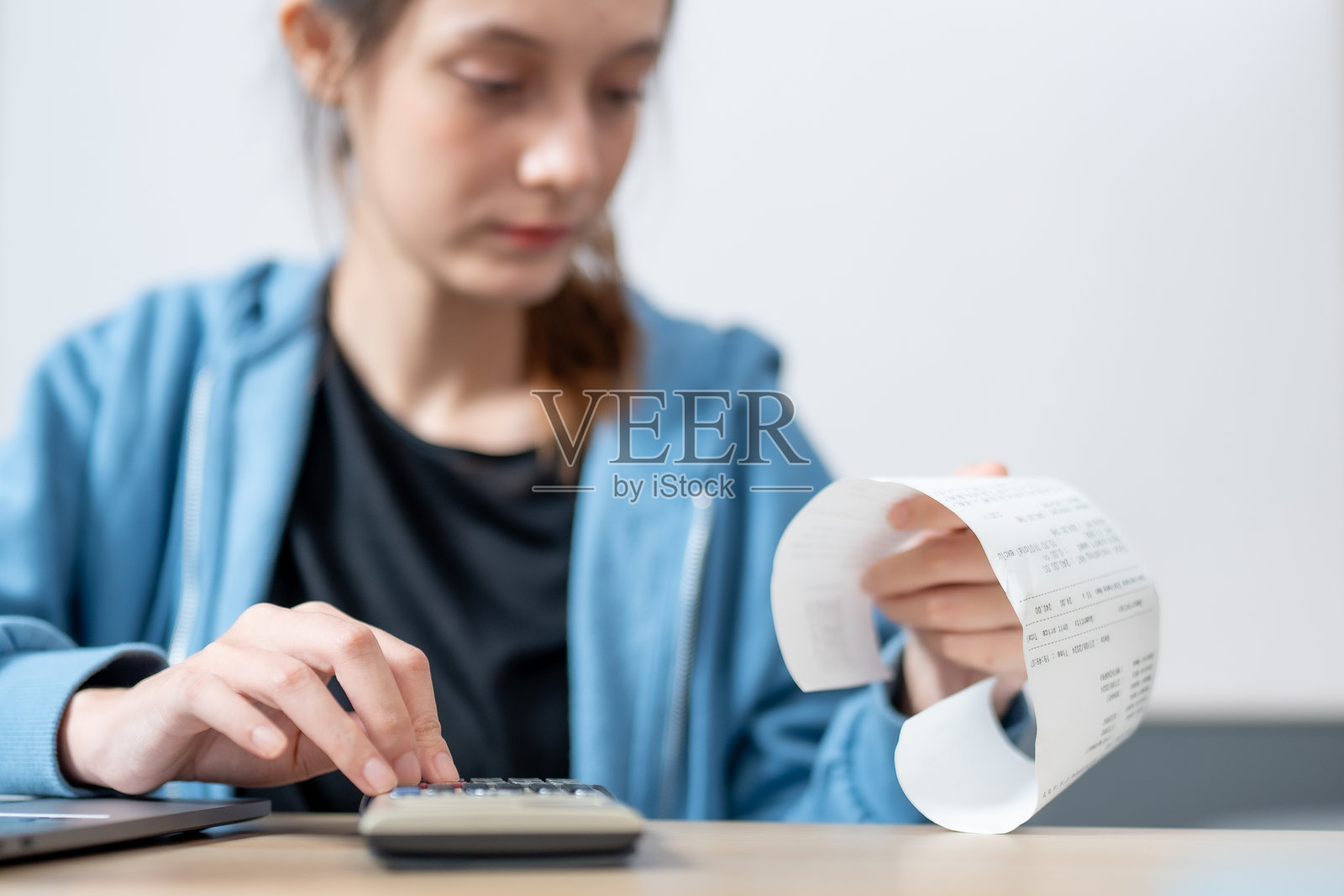 年轻女性使用计算器计算开支并查看收据,专注于预算。这一场景捕捉了财务管理和组织的本质。照片摄影图片