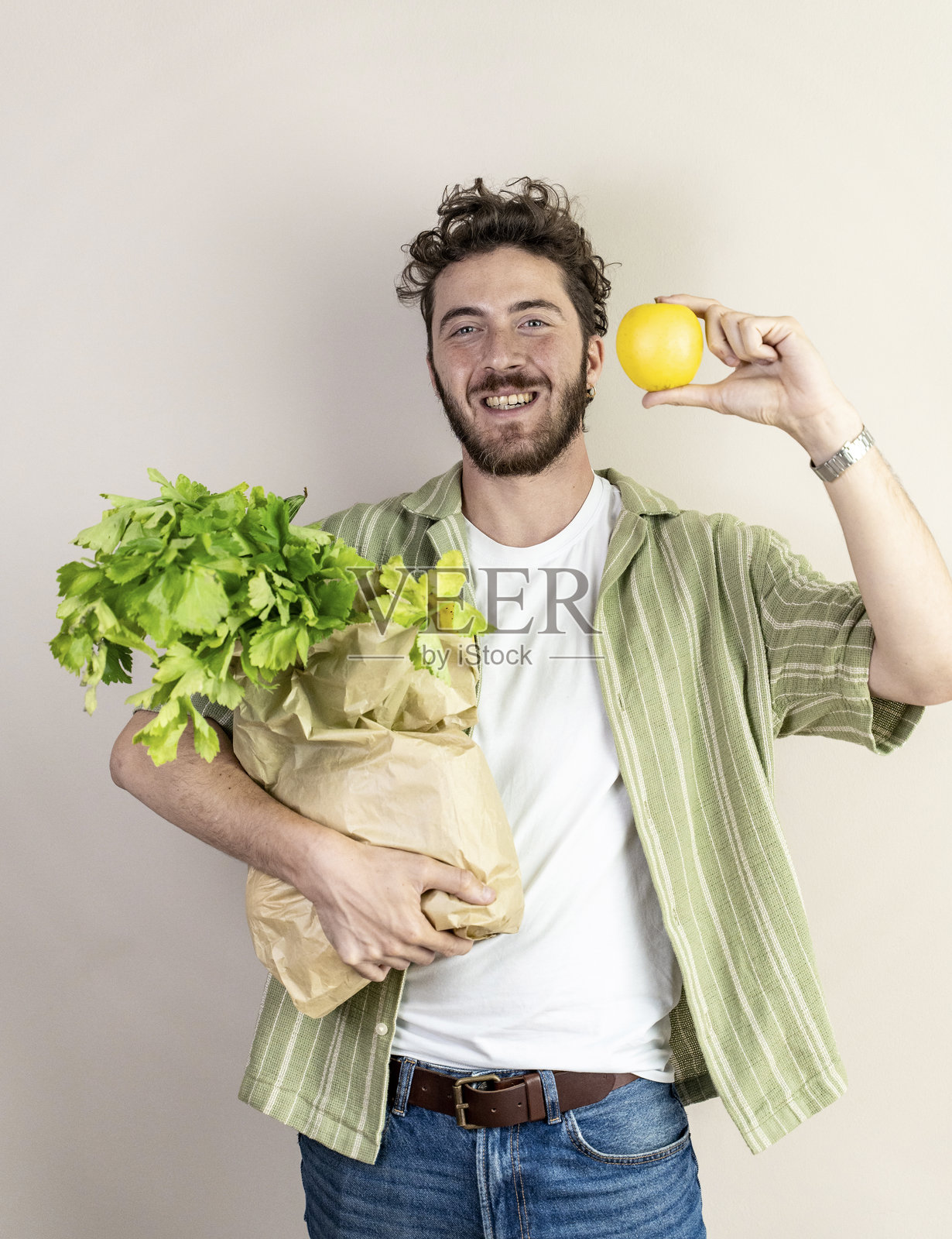 健康的年轻男子手持环保购物袋,里面装有新鲜的绿叶蔬菜和一个黄色苹果照片摄影图片