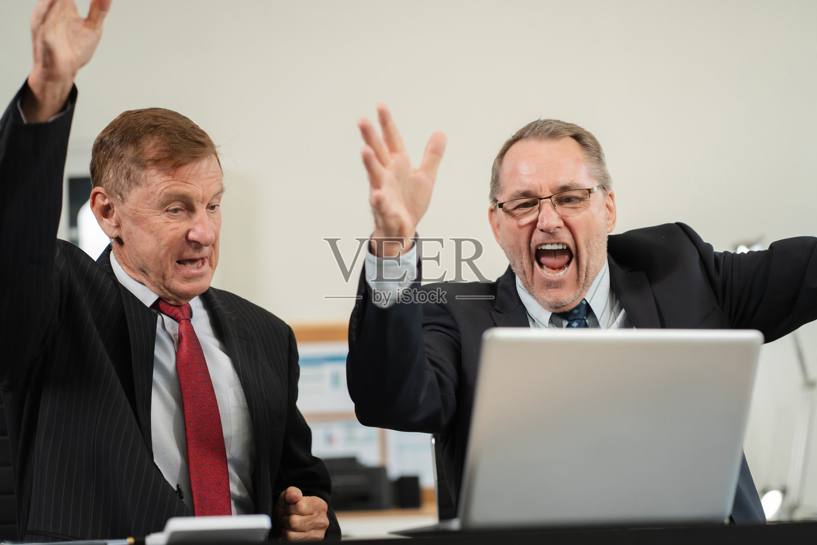 成功的商业团队,兴奋的成熟商人双臂交叉,展现积极情绪,在现代办公室愉快地使用电脑工作。照片摄影图片