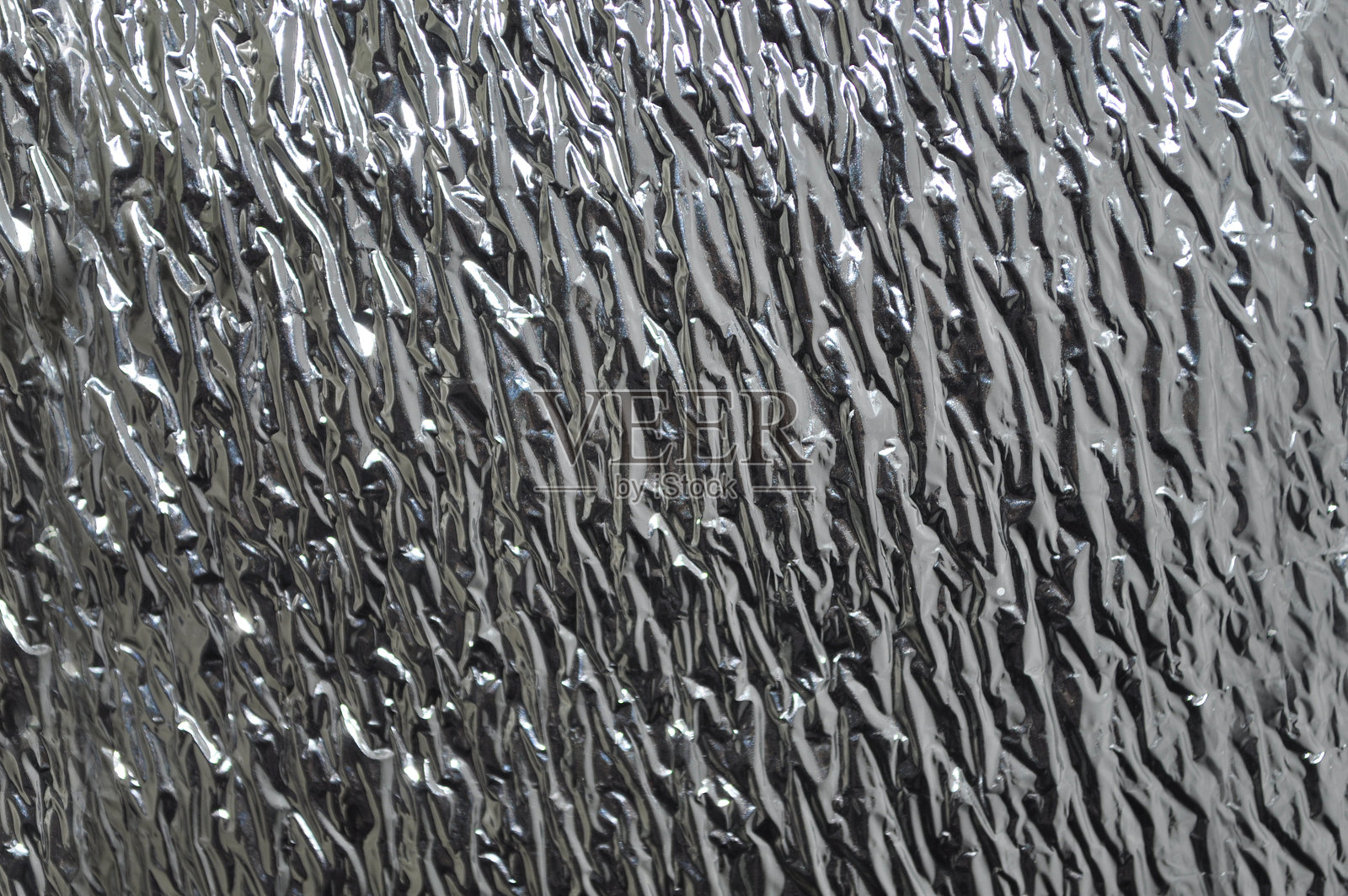 闪亮的金属皱纹表面,带有对角纹理。反光箔材料形成抽象的工业图案。照片摄影图片