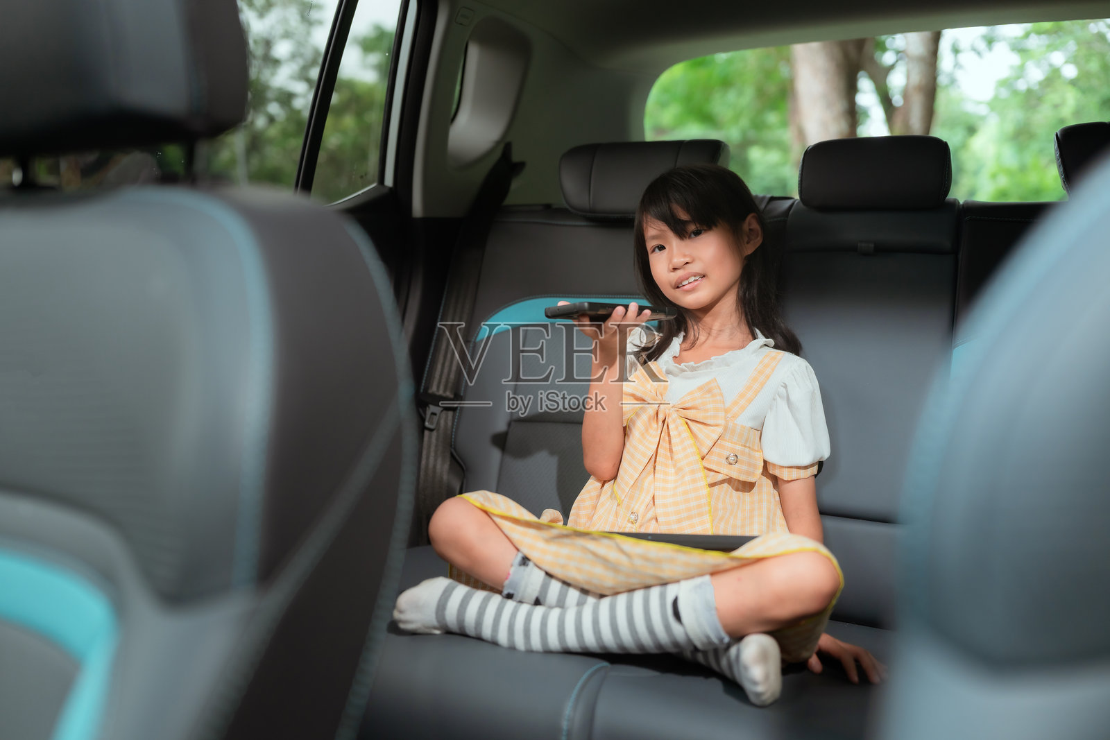 年轻女孩在阳光明媚的下午旅行中,坐在车后座上享受平板电脑。照片摄影图片