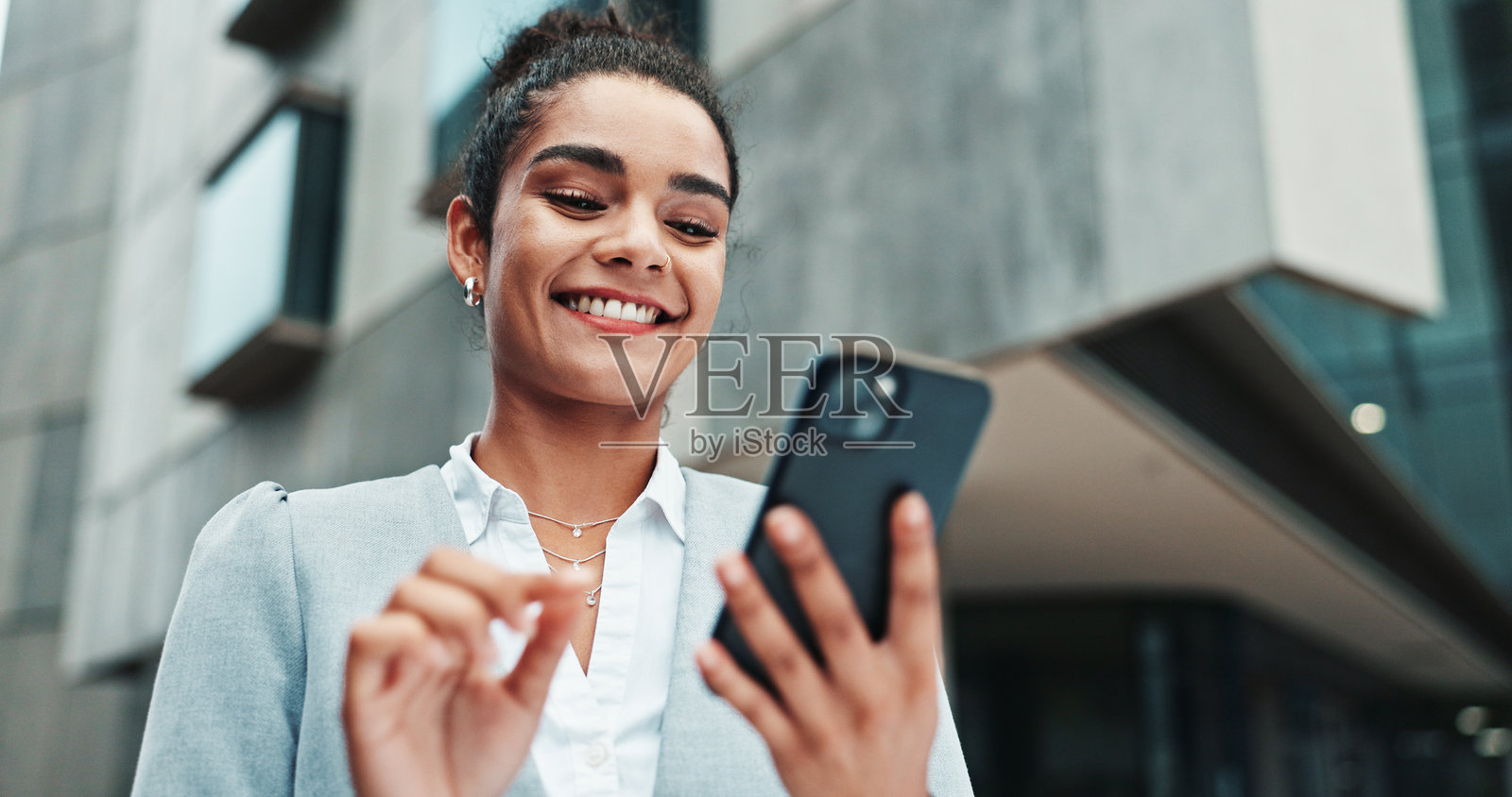 城市中的商务女性,手持手机,快乐地旅行,涉及房地产、互联网或连接。在线企业家进行社交媒体网络,使用应用程序列出房产或通过短信联系房地产经纪人。照片摄影图片