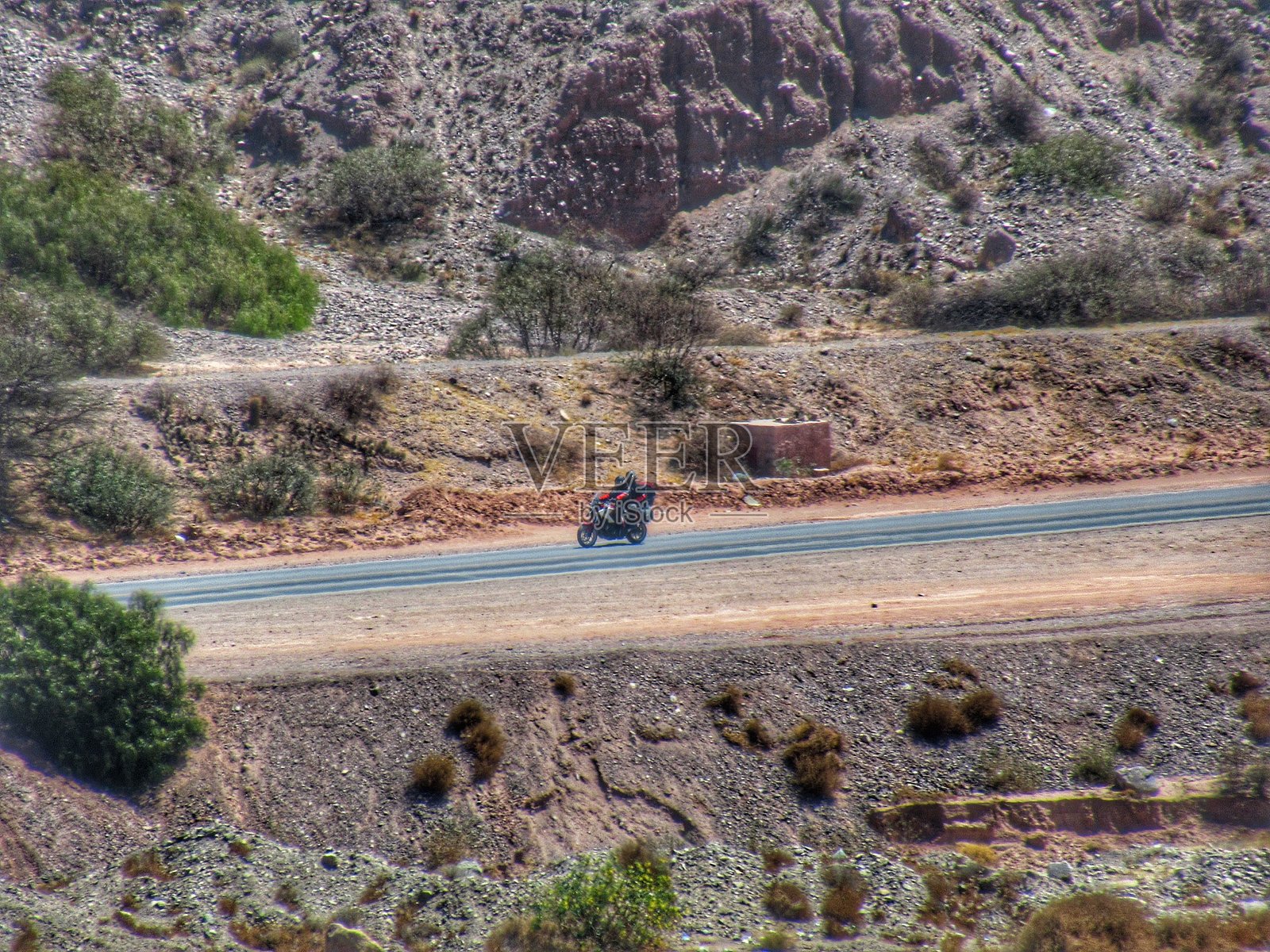 一对情侣在阿根廷北部胡胡伊省的蒂尔卡拉市的阳光明媚、蓝天的铺装公路上骑摩托车旅行。照片摄影图片