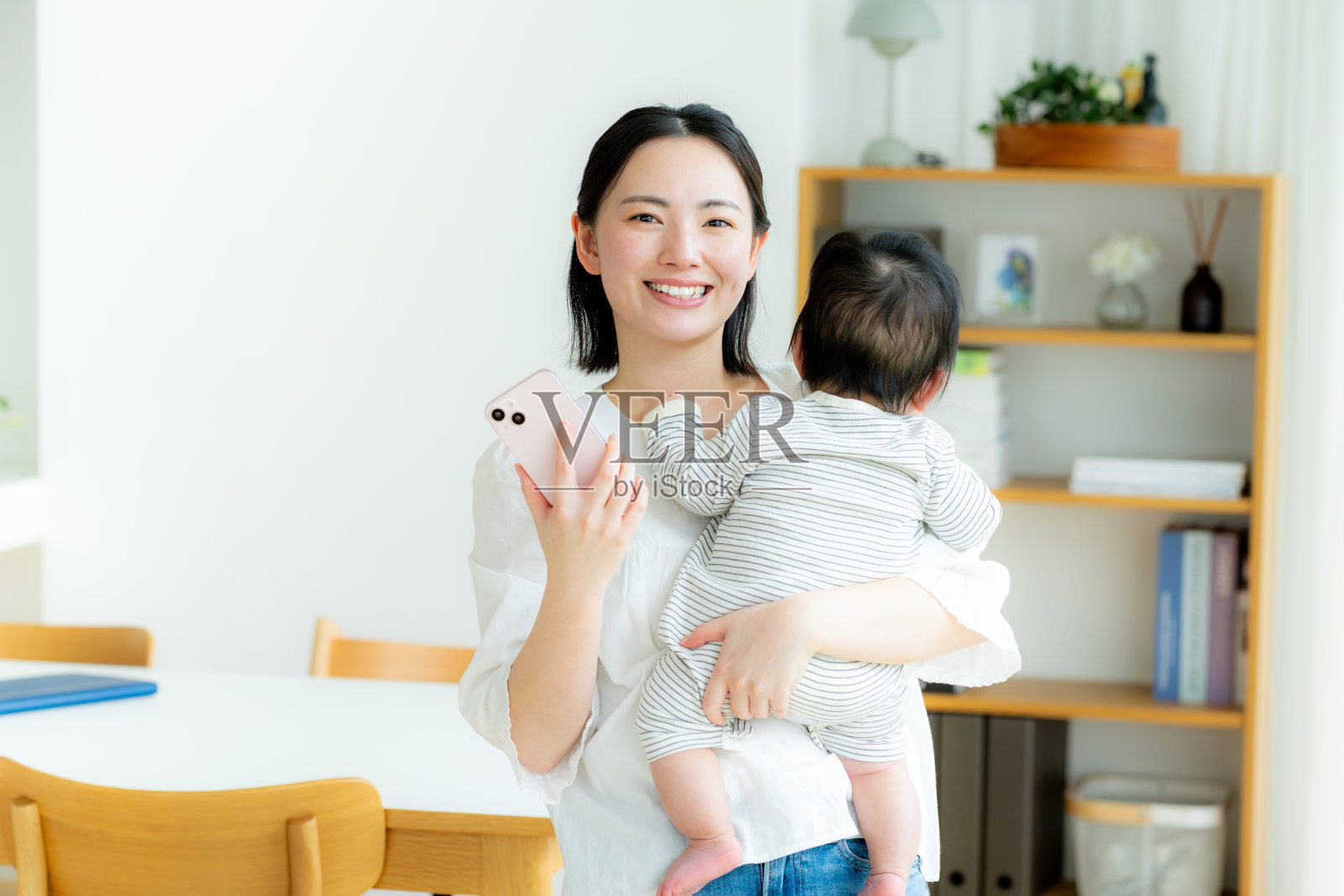 妈妈抱着婴儿,同时拿着智能手机照片摄影图片