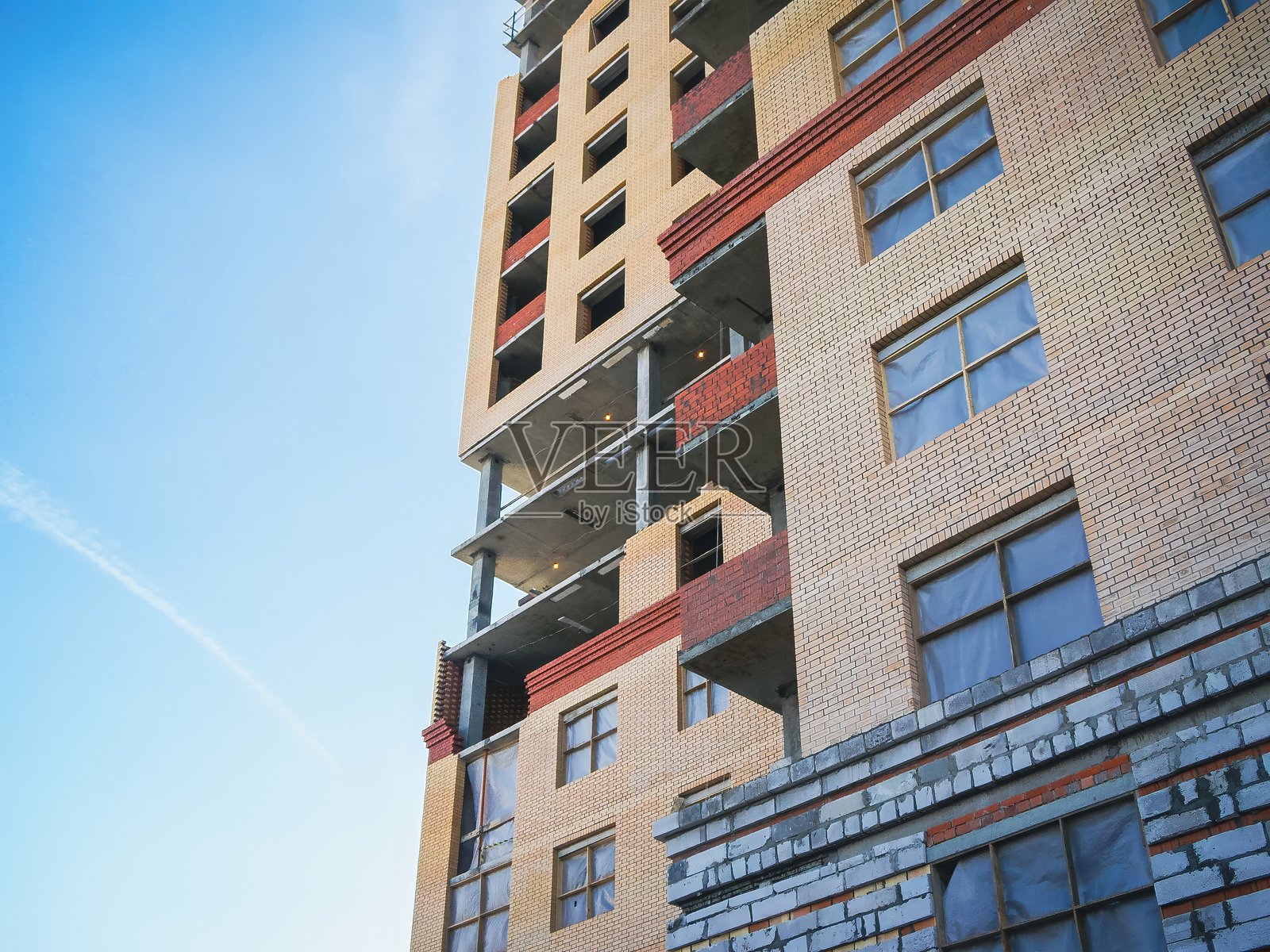 低角度拍摄一座正在建设中的建筑,背景是明亮的蓝天,建筑材料混合了砖块。照片摄影图片