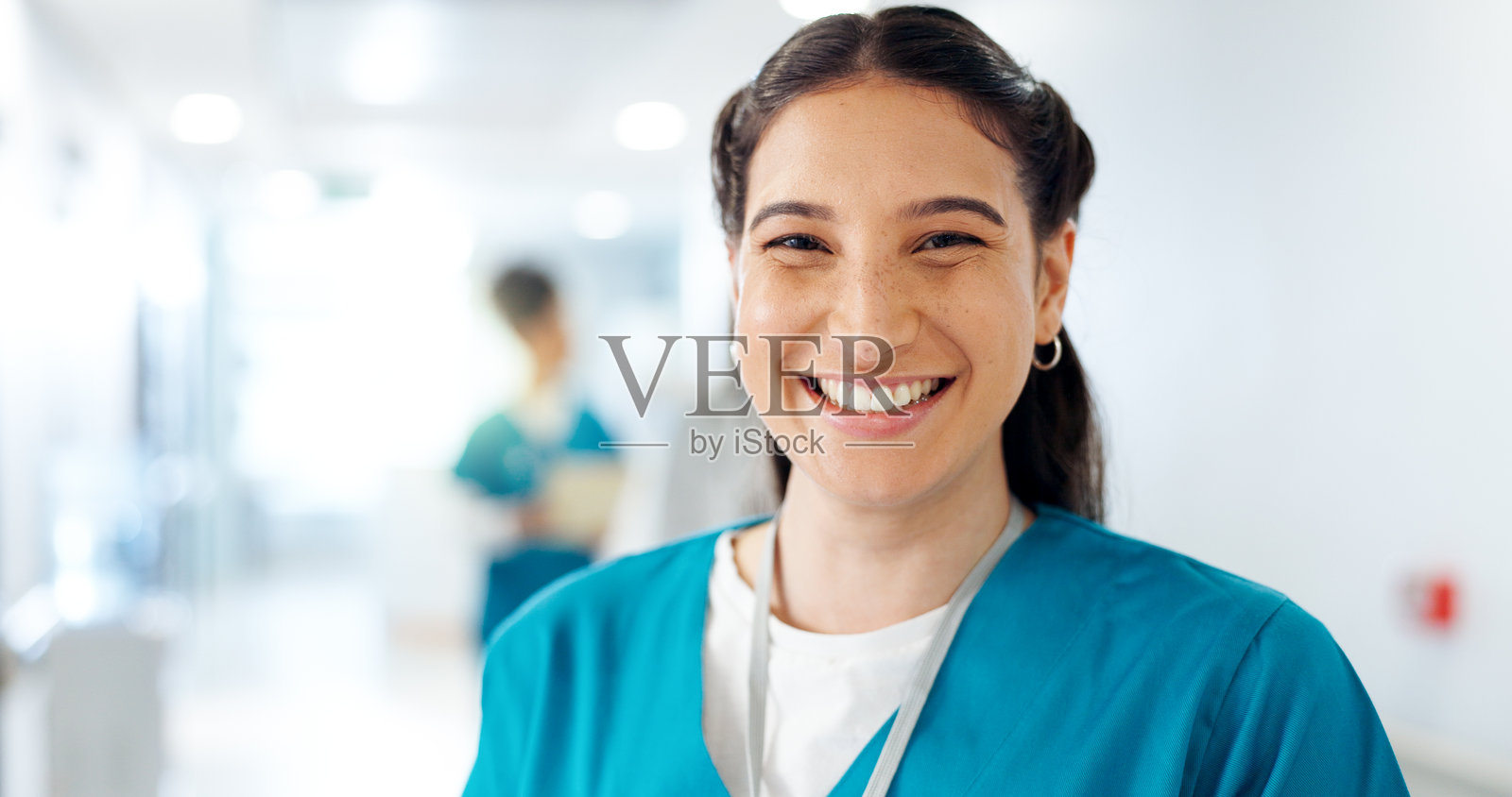 快乐的女性护士在医院走廊的肖像,展现出对医疗职业发展的自豪感。微笑的女性医疗工作者在护理诊所走廊中充满自信。照片摄影图片