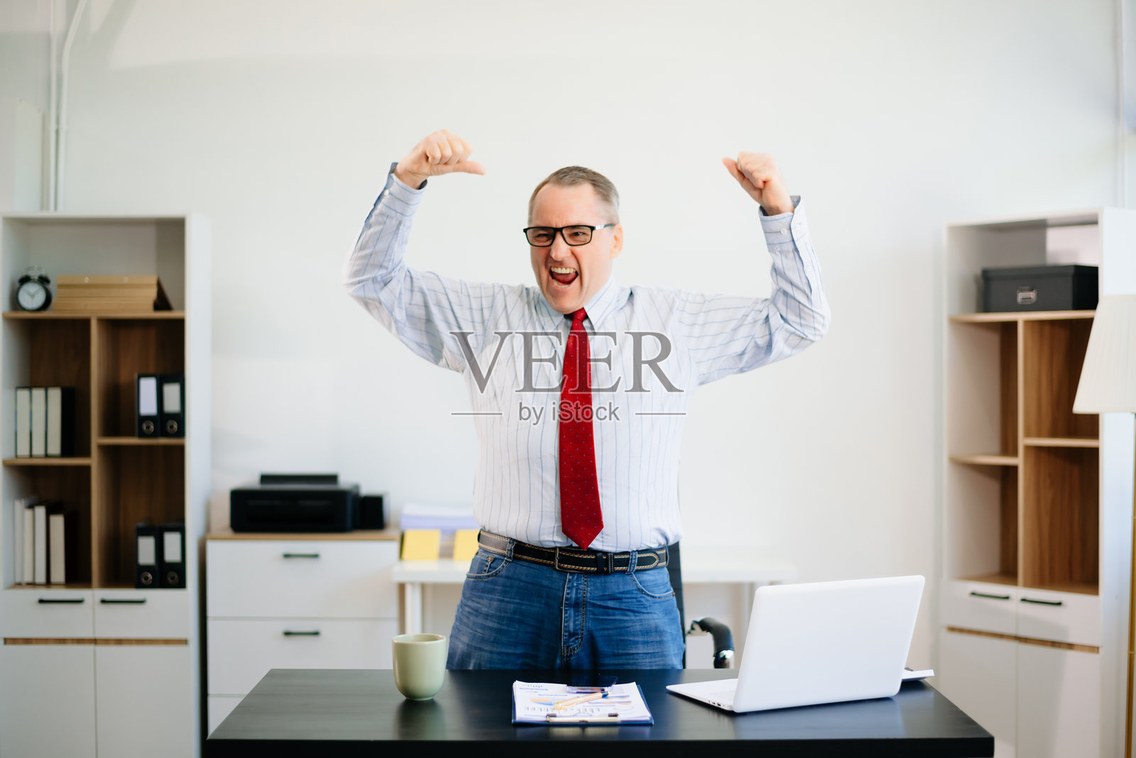 成熟的商人在办公室桌子上穿着红色领带,专注而紧张地使用笔记本电脑。企业、金融、科技和职场压力。照片摄影图片