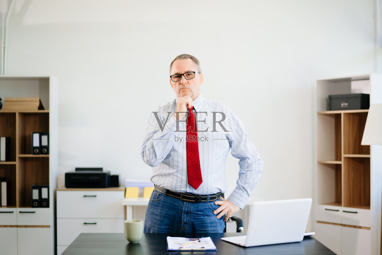 成熟的商人在办公室桌子上穿着红色领带,专注而紧张地使用笔记本电脑。企业、金融、科技和职场压力。照片摄影图片