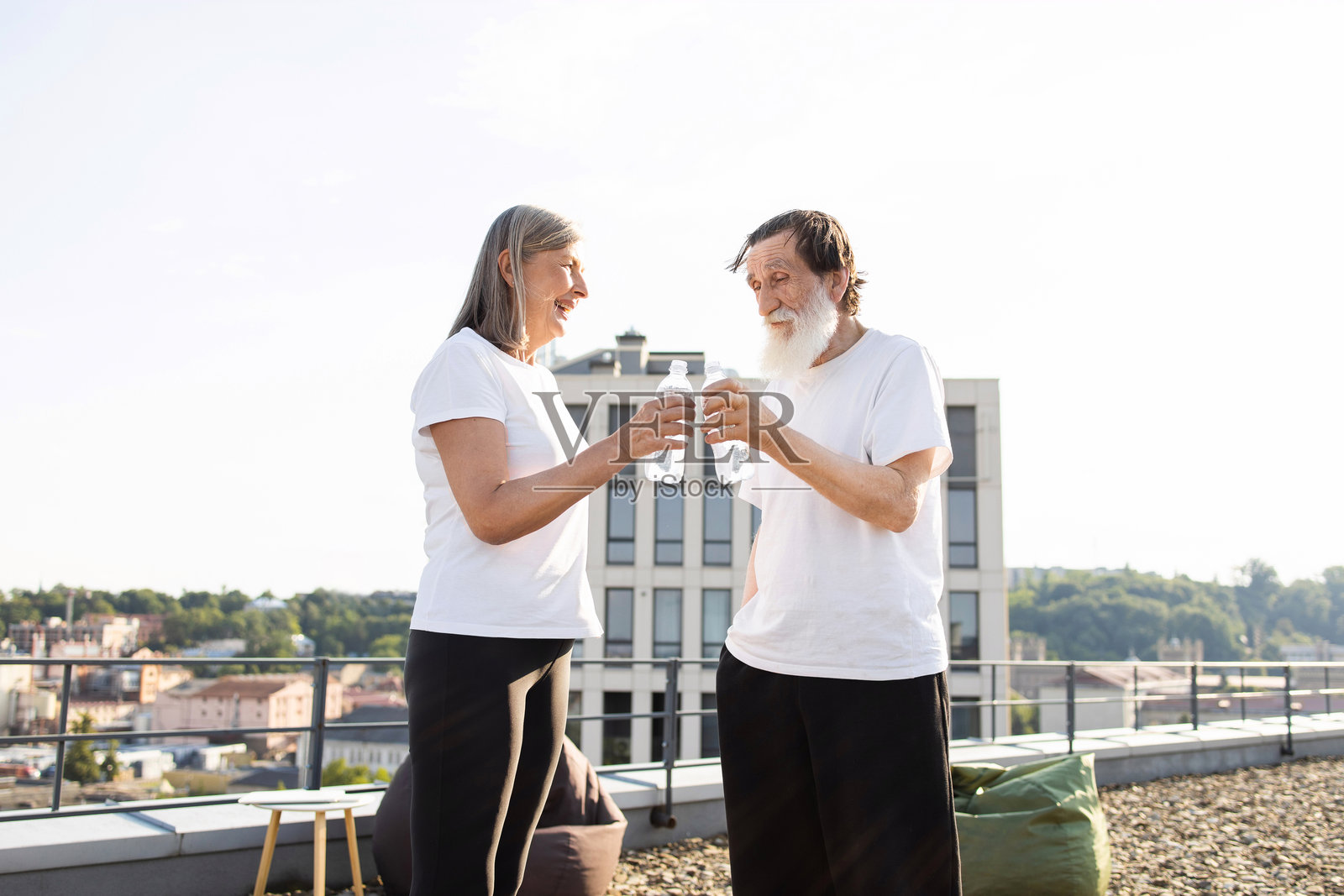 老年夫妇在屋顶露台上享受水,刚刚完成锻炼。照片摄影图片