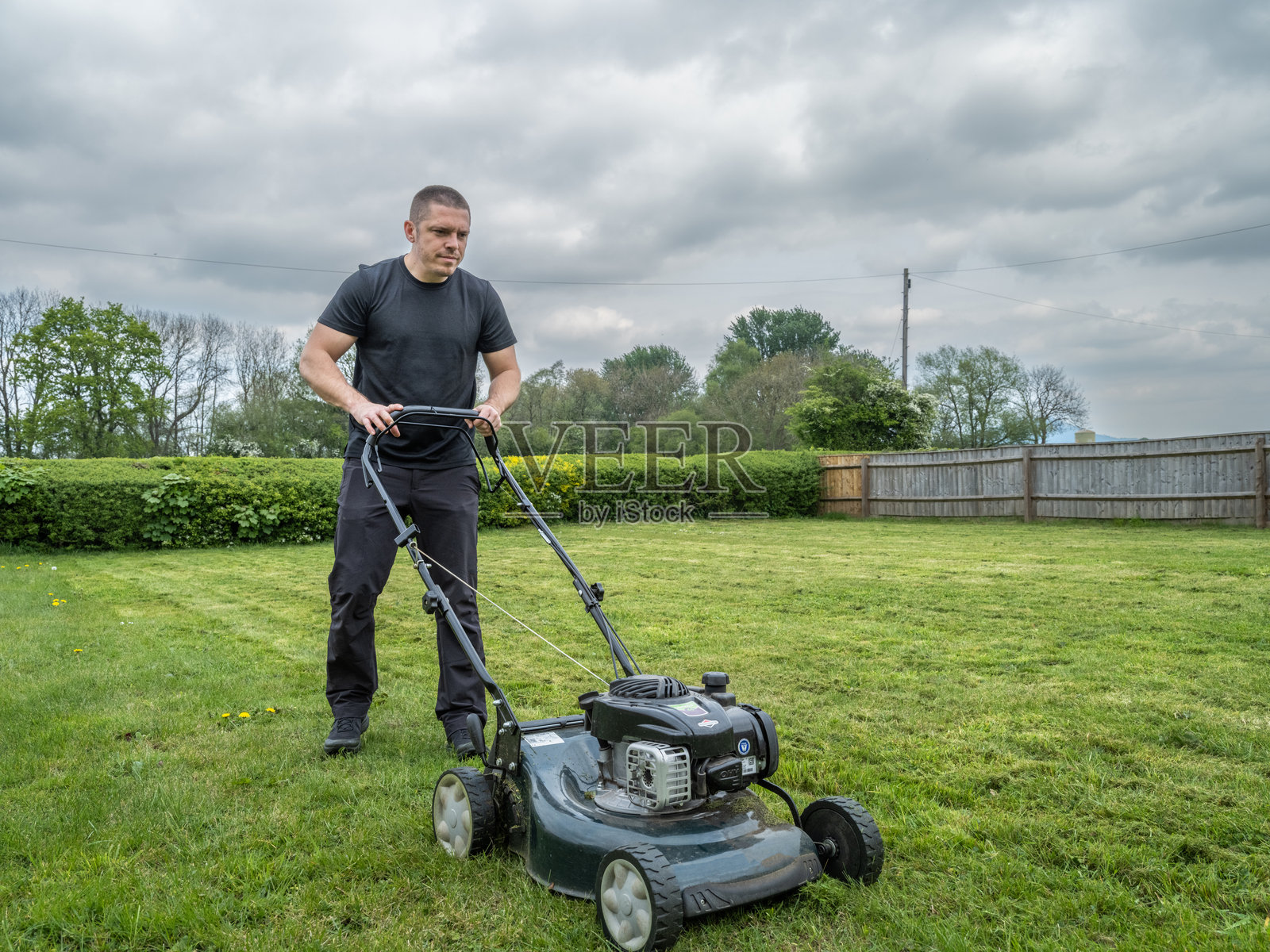 阴天里修剪草坪的男人照片摄影图片