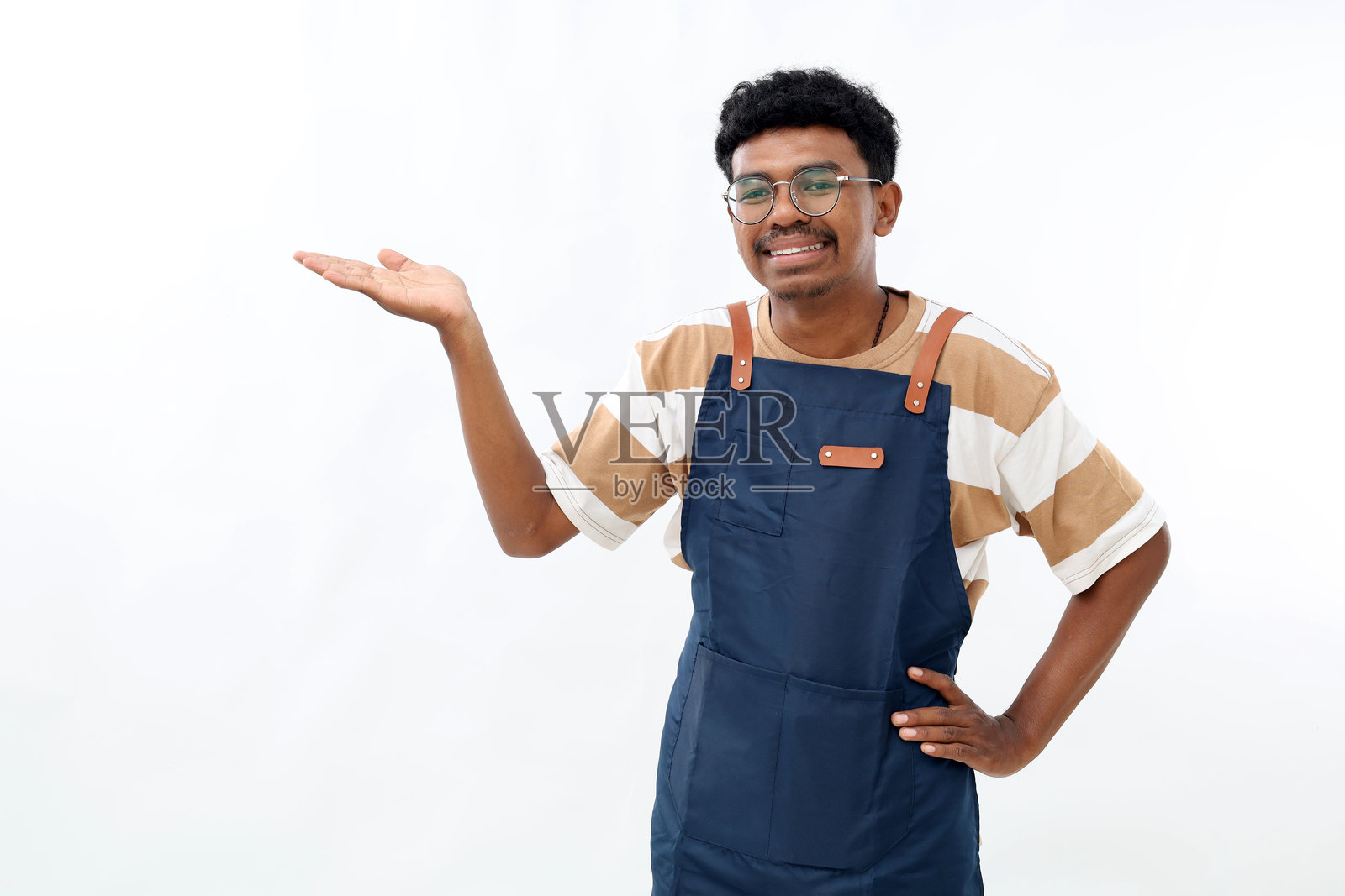 微笑的亚洲男子穿着厨房围裙,手里拿着某物,背景为白色。设计的样板。照片摄影图片