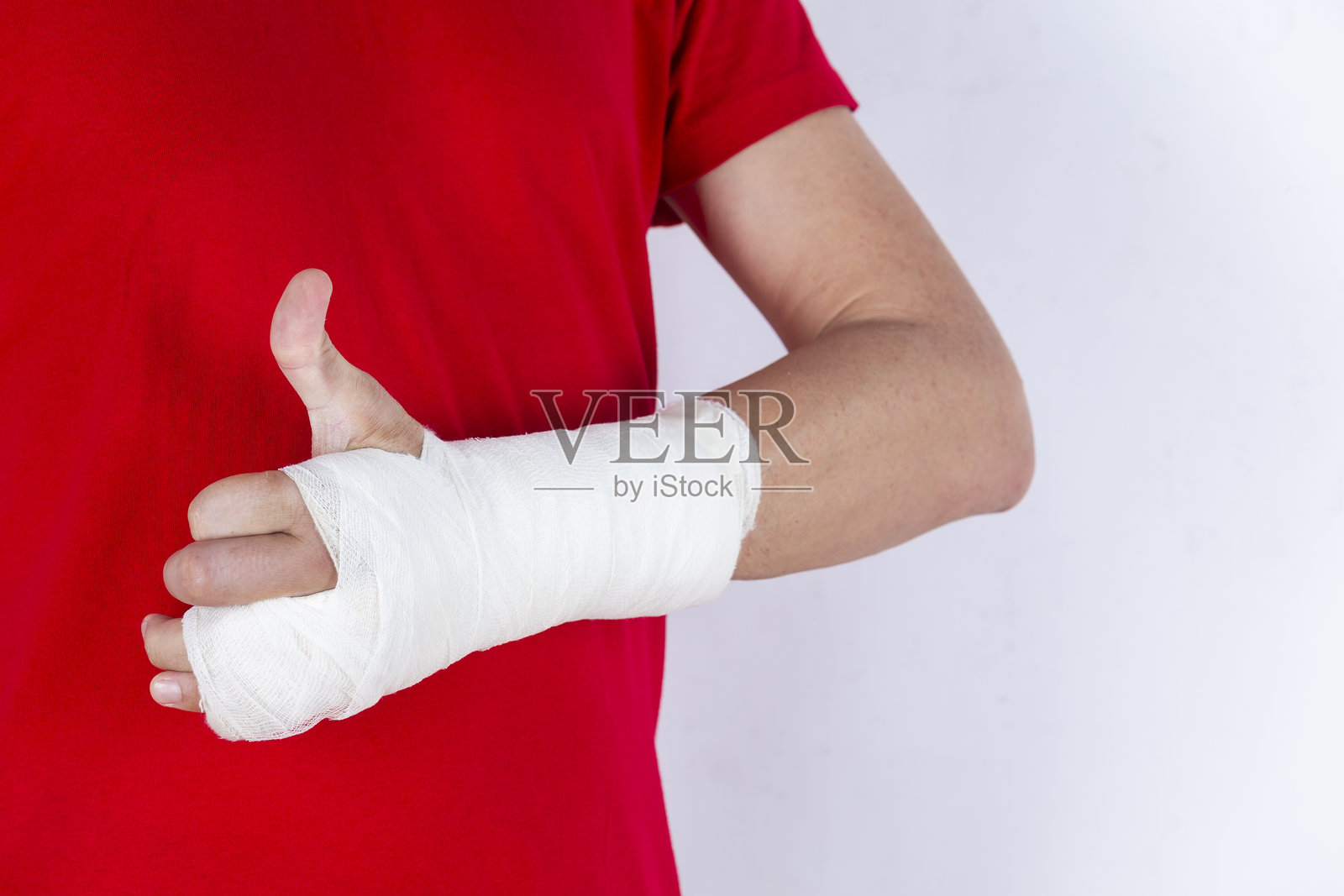 医学概念。穿红色衬衫的白人男性的身体部位特写,手部骨折,包着石膏和创可贴,背景为白色。照片摄影图片