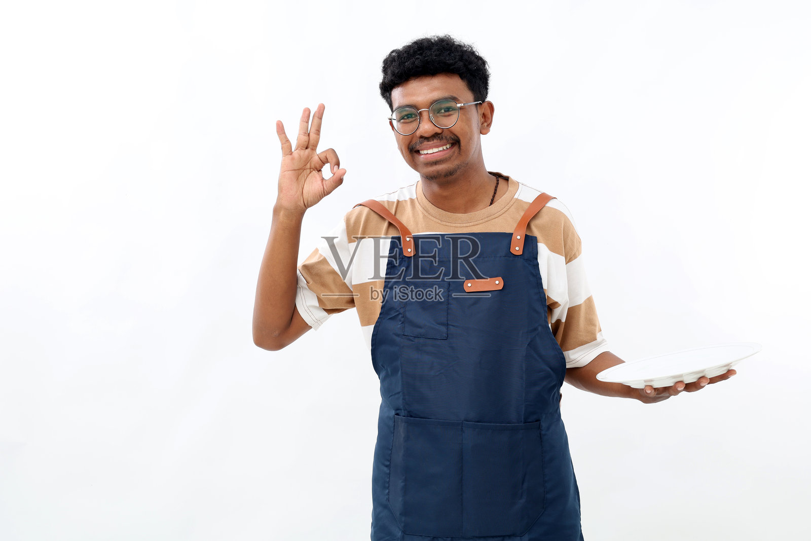 年轻亚洲男性厨师在白色背景下做出“好”的手势,手中拿着空盘子。照片摄影图片