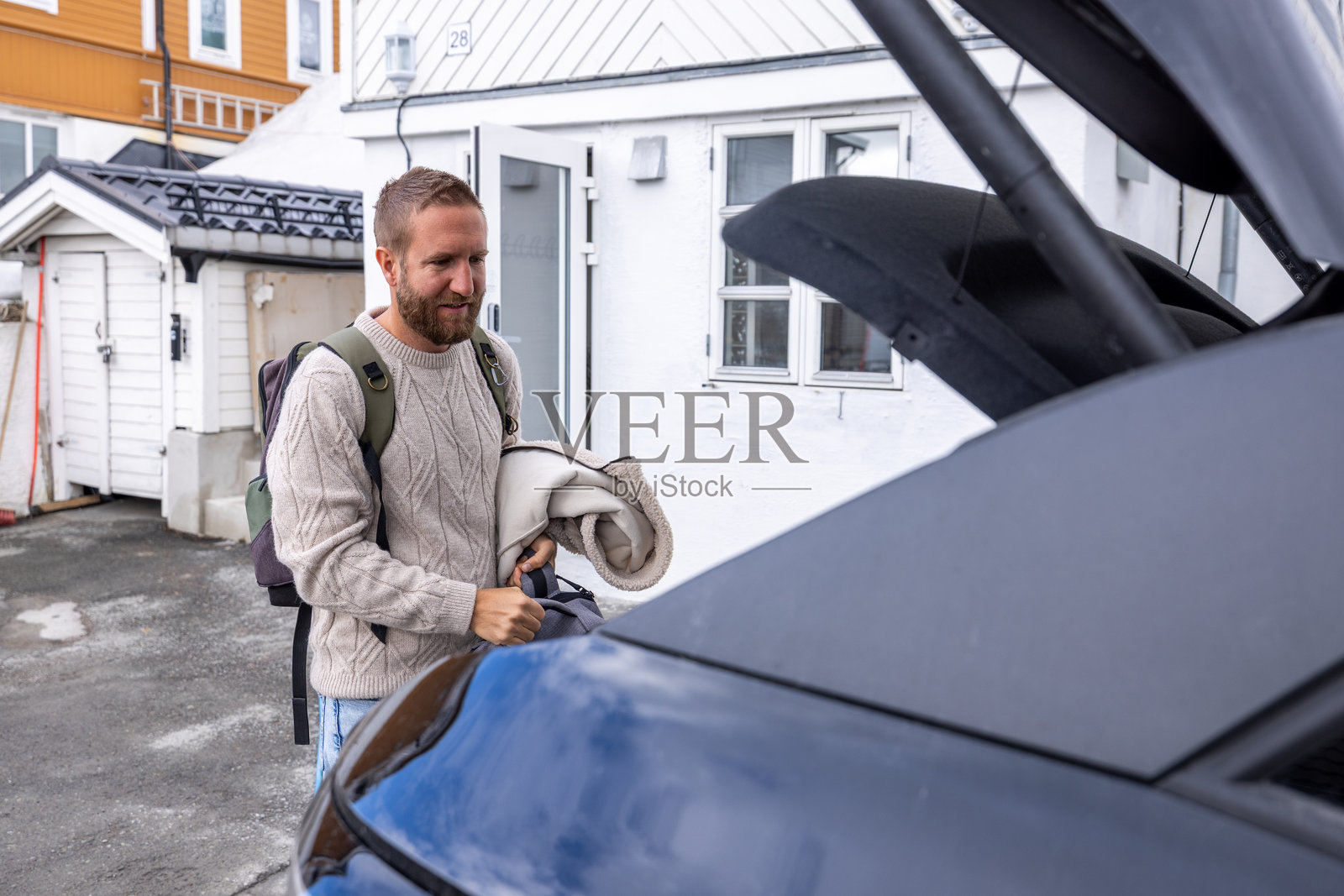 男子在住宅车道上用毯子打包汽车后备箱照片摄影图片