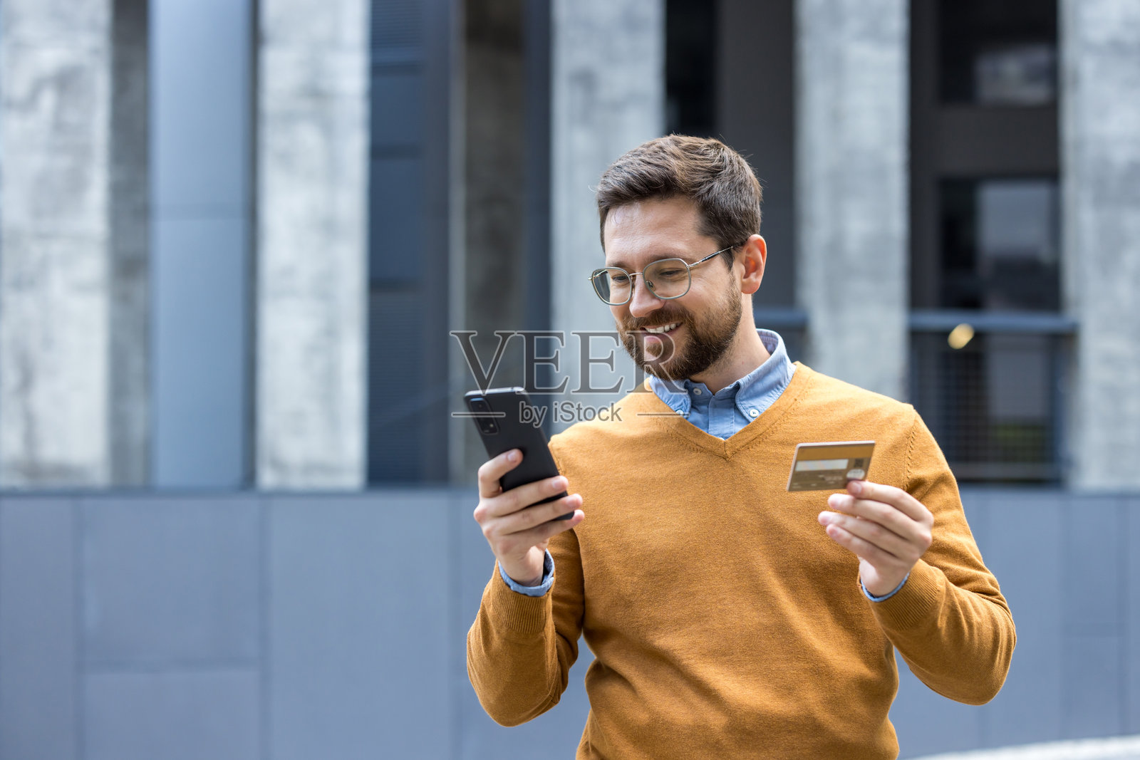 年轻男子在户外特写,手持信用卡并使用手机照片摄影图片