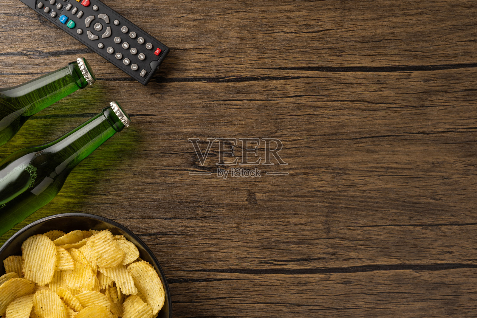 在家悠闲的晚上,啤酒瓶、遥控器和薯片伴随星空。照片摄影图片