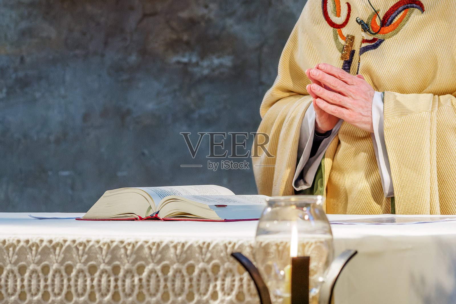 天主教神父在弥撒期间双手合十祈祷,站在祭坛上照片摄影图片