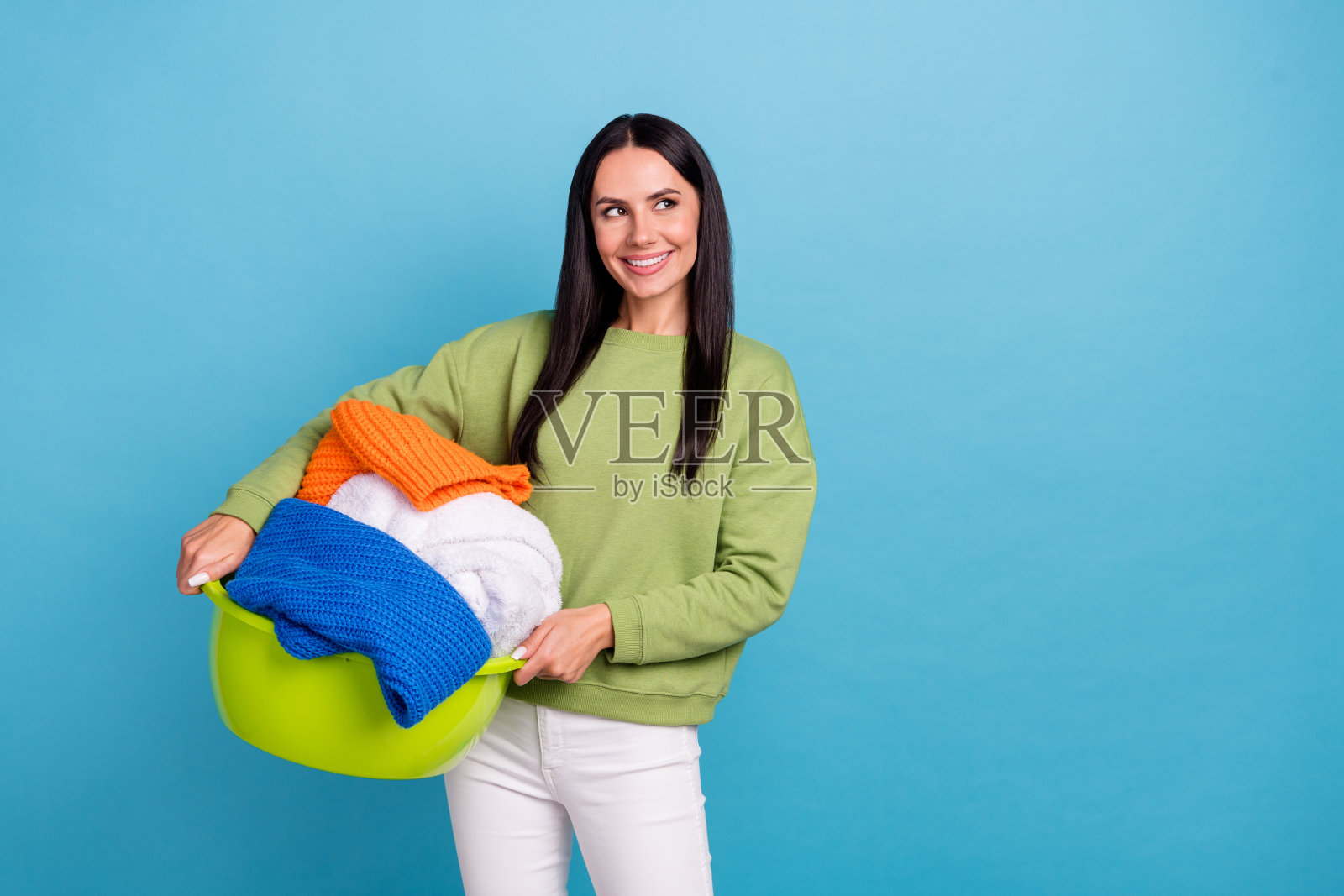 年轻的心情愉快的女佣看着空旷的空间,看到洗涤剂促销,背景为蓝色。照片摄影图片