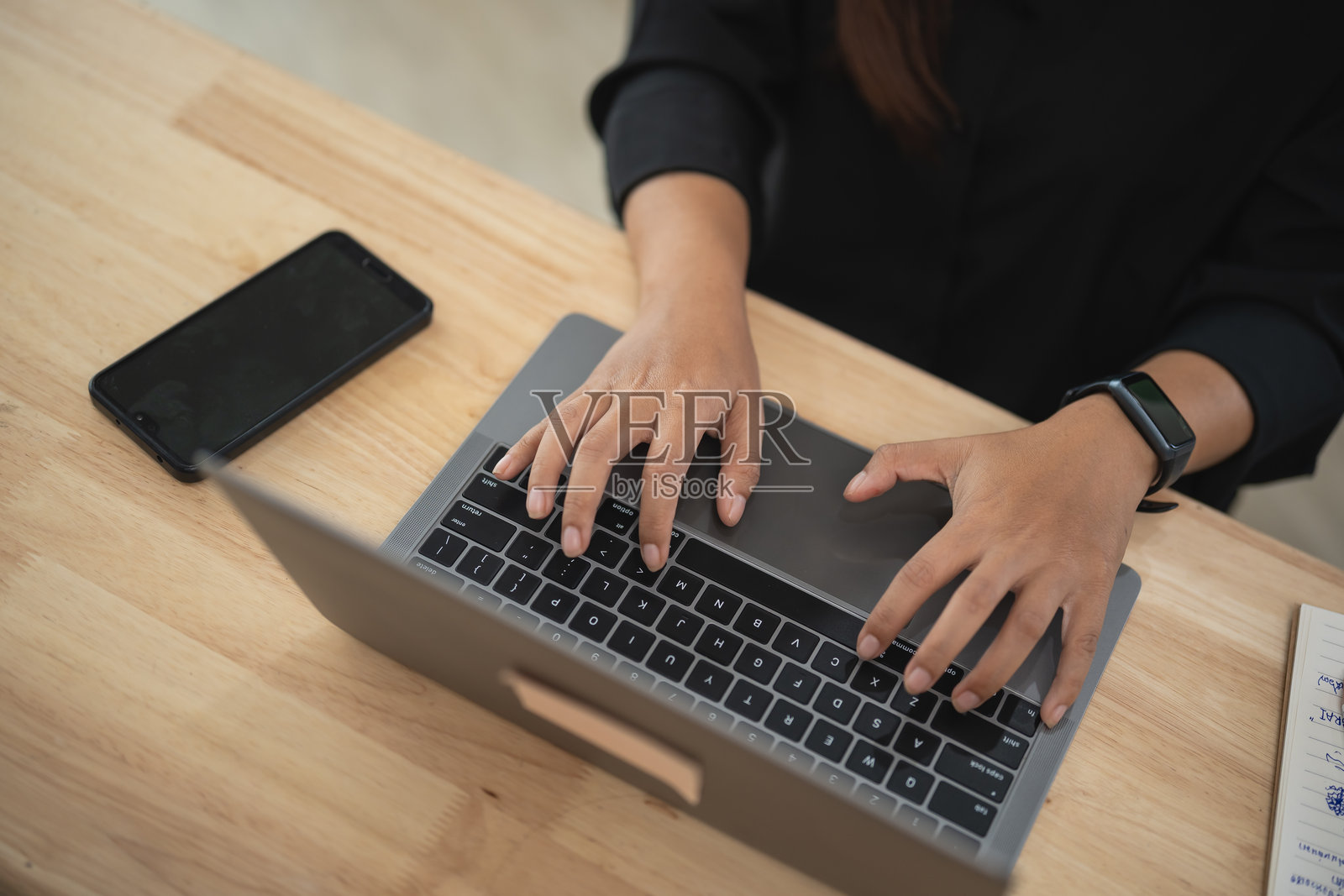 明亮办公室环境中,手部特写在笔记本电脑键盘上打字,旁边有智能手机,展示现代工作文化。照片摄影图片