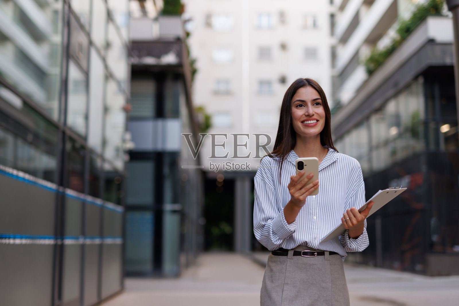 职业女性在城市街道上走,查看智能手机,手里拿着文件夹照片摄影图片