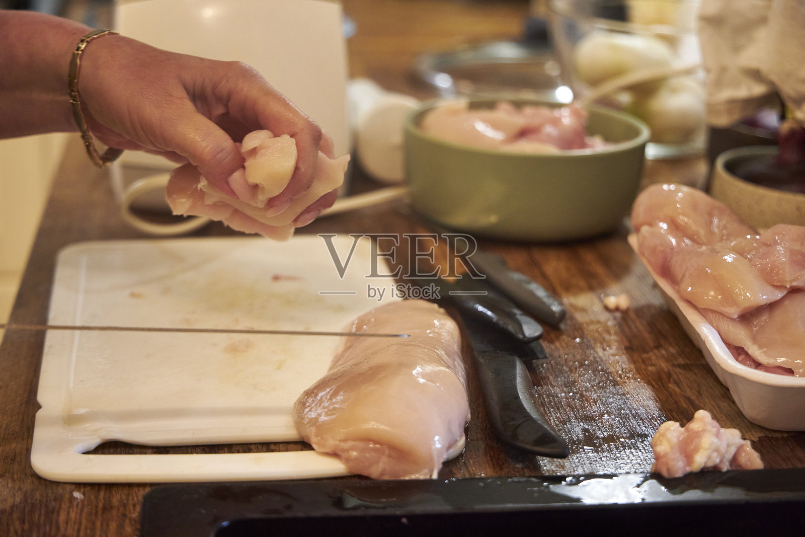 特写镜头显示一位女性在厨房的白色切菜板上将生鸡胸肉切成块。该图像捕捉了一个食品准备的瞬间,强调健康烹饪、清洁和家庭生活。照片摄影图片