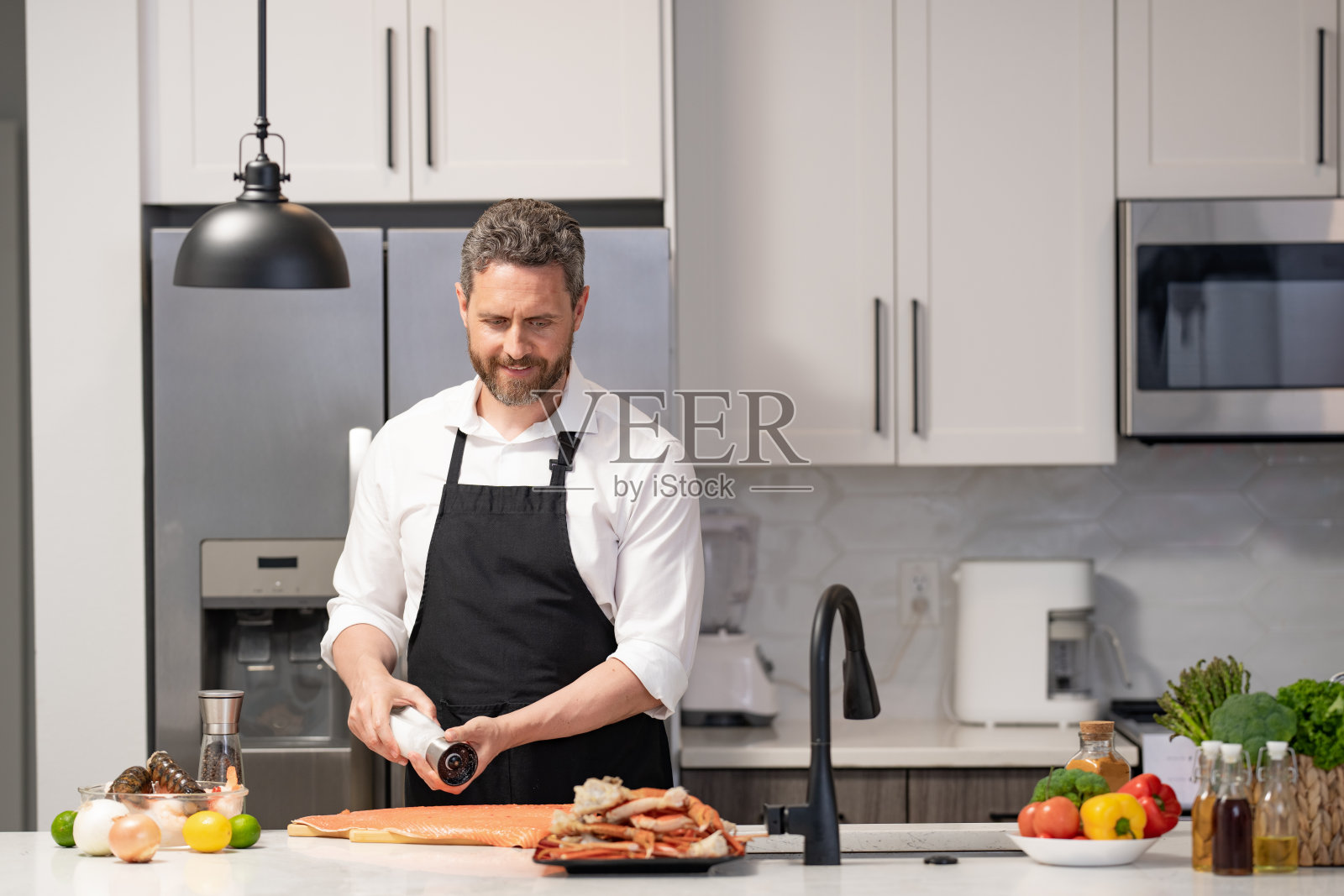 男人在厨房烹饪美味的蟹腿。健康饮食。男人在烹饪美味的餐点。家庭菜单上的海鲜。西班牙裔男人在厨房准备海鲜。新鲜海鲜。照片摄影图片