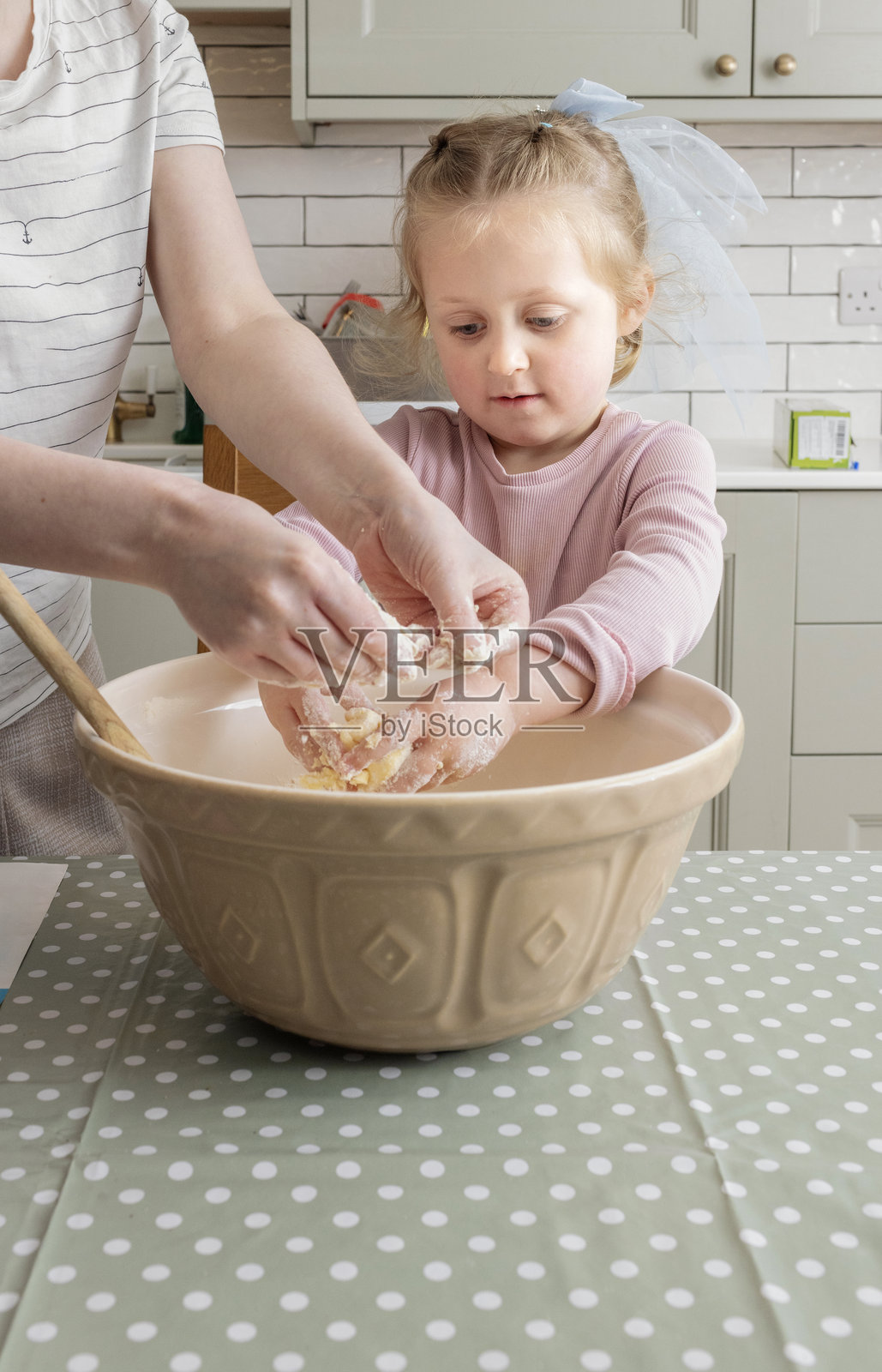年轻妈妈和她的小女儿在厨房桌子上搅拌黄油,准备制作果酱饼干。照片摄影图片