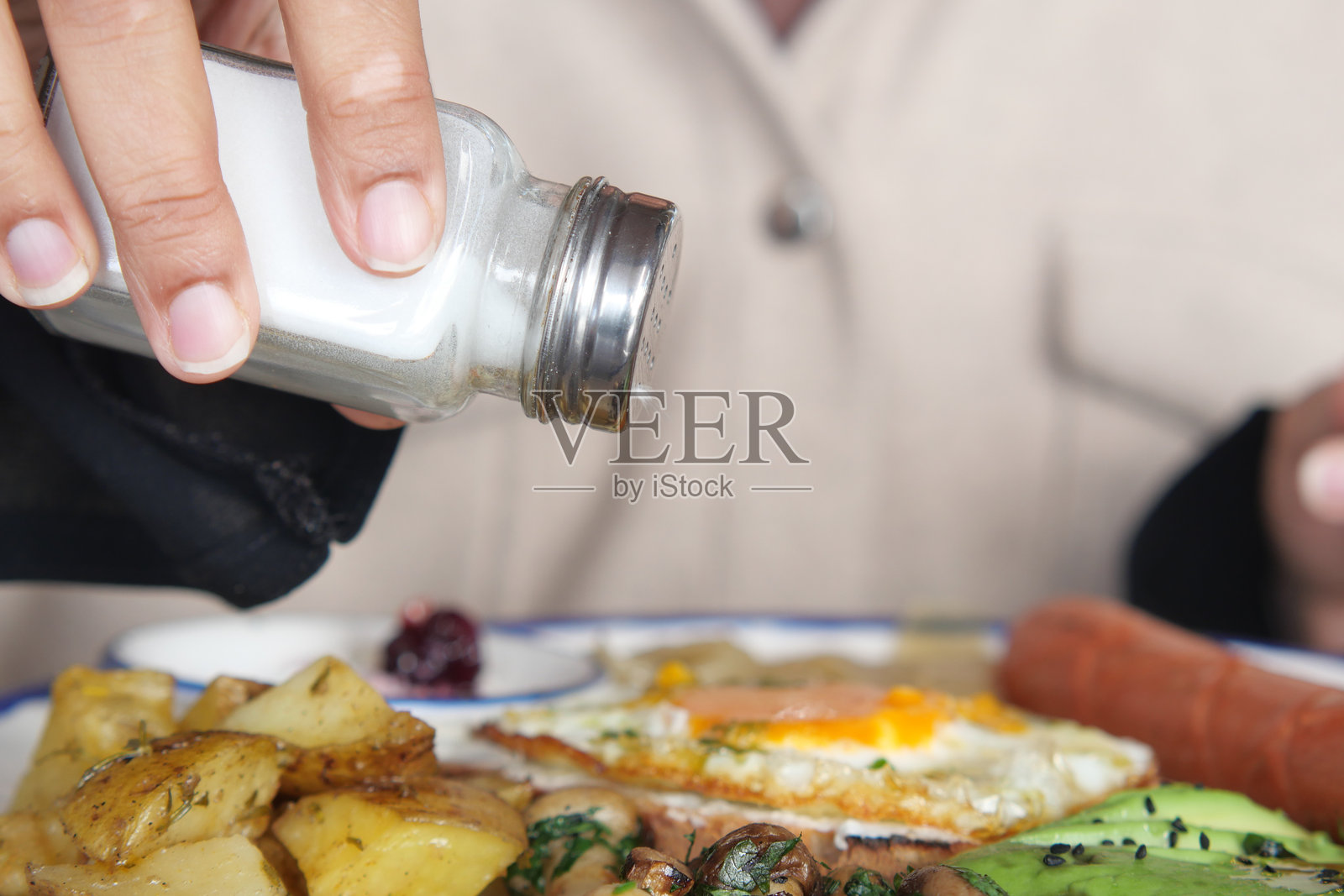 早晨的阳光下,人在早餐盘上撒盐调味。照片摄影图片