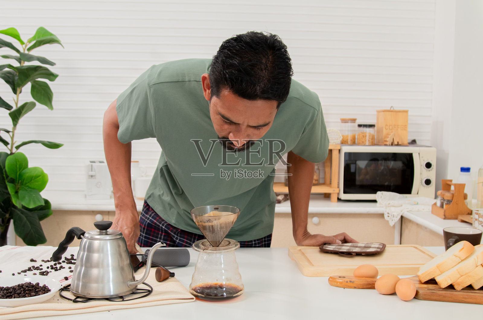 中年有胡子的亚洲男子闻着自己烘焙的咖啡香气。享受早晨咖啡。早晨的美味与甜蜜。在家度假的生活方式概念。照片摄影图片