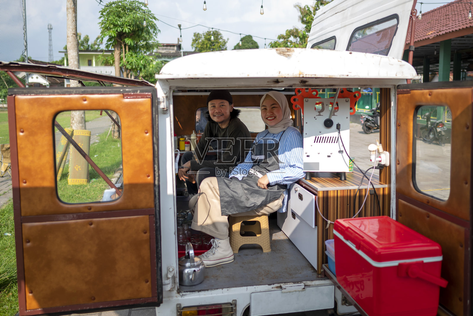 东南亚印尼男性与身穿头巾的中国穆斯林女性情侣在咖啡店内担任咖啡师。一个小型咖啡店或咖啡车的生意。照片摄影图片