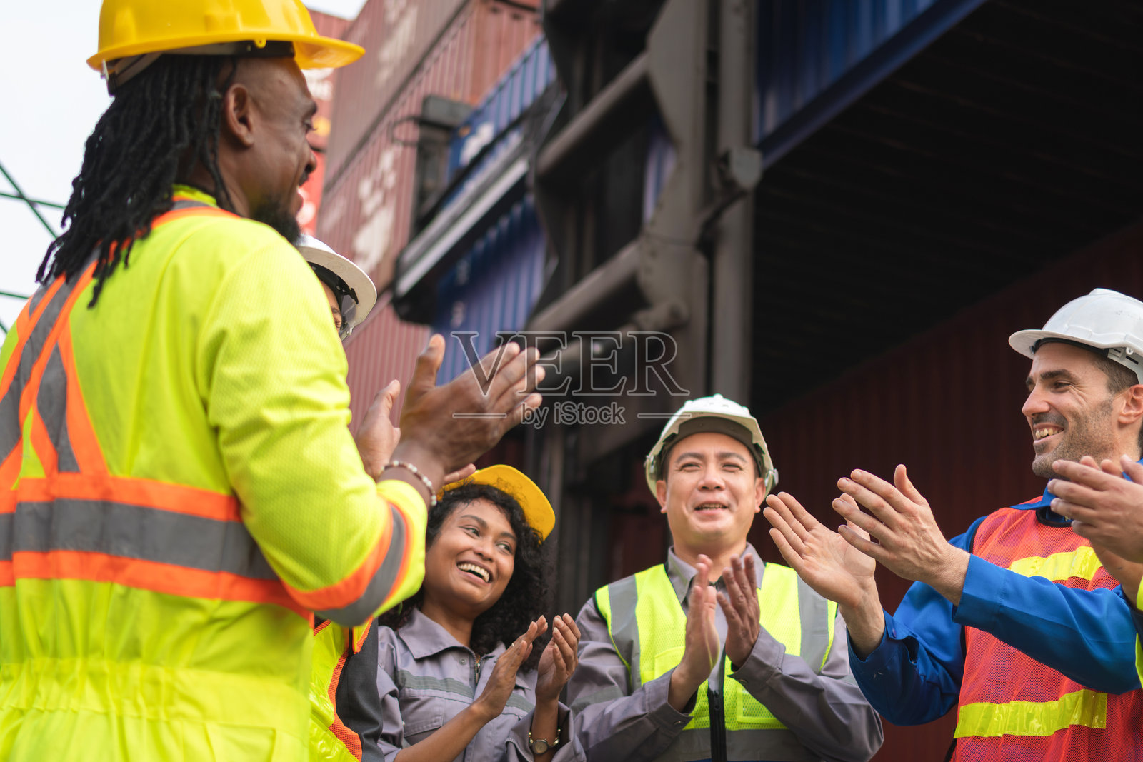 快乐的多元化工业工人们一起鼓掌,来自不同文化背景的工程师和劳工团队庆祝成功,微笑的同事们穿着安全帽和马甲在户外鼓掌。照片摄影图片