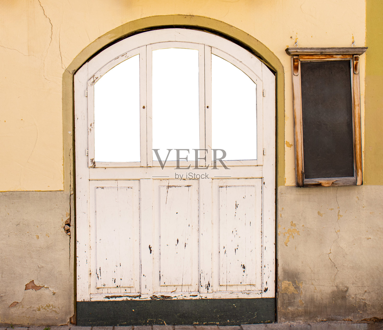老旧的拱形木门,白漆剥落,旁边有一个复古的墙壁公告板,欧洲街道。照片摄影图片