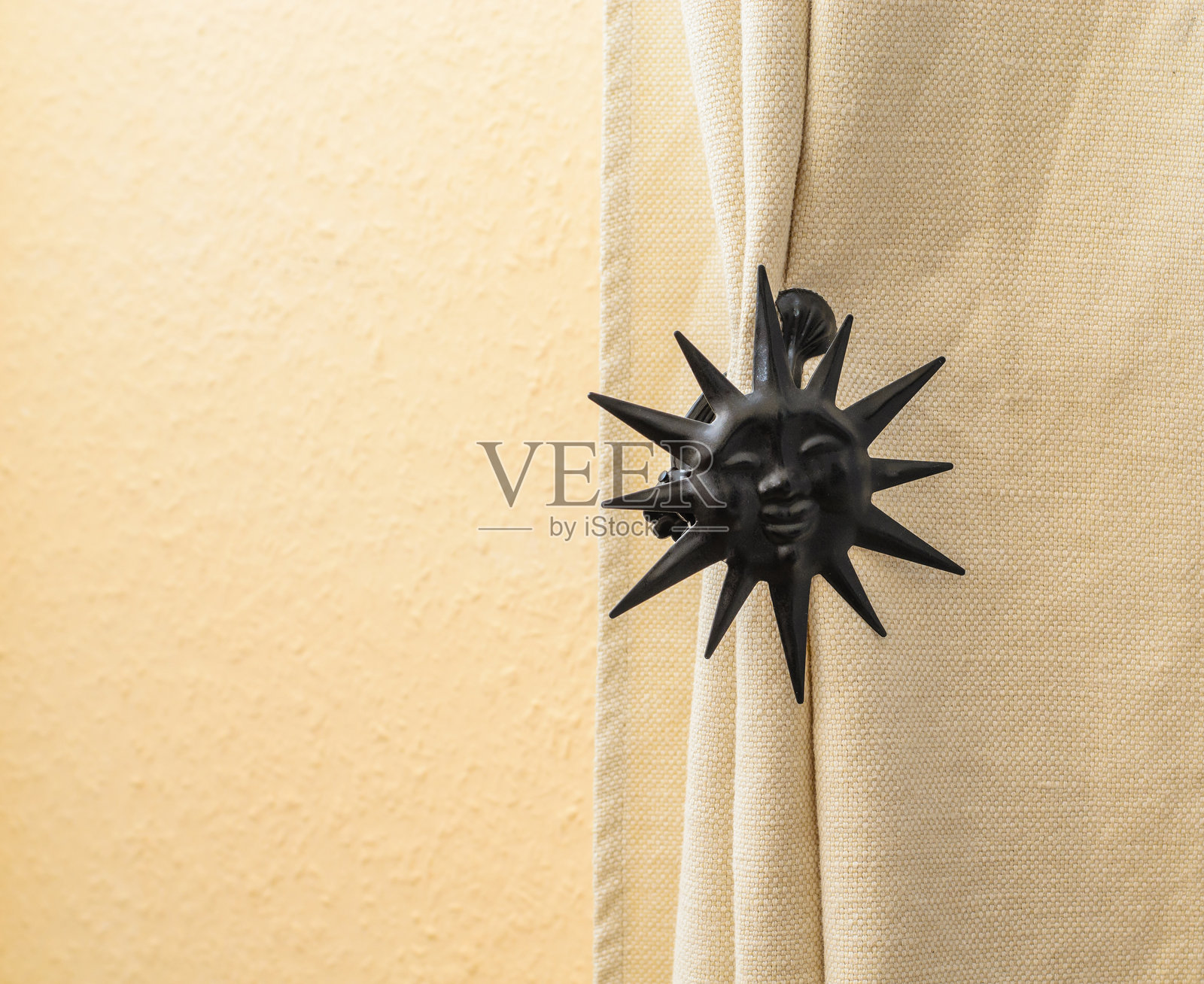 黑色太阳形状的窗帘绑带装饰,固定着米色窗帘。照片摄影图片