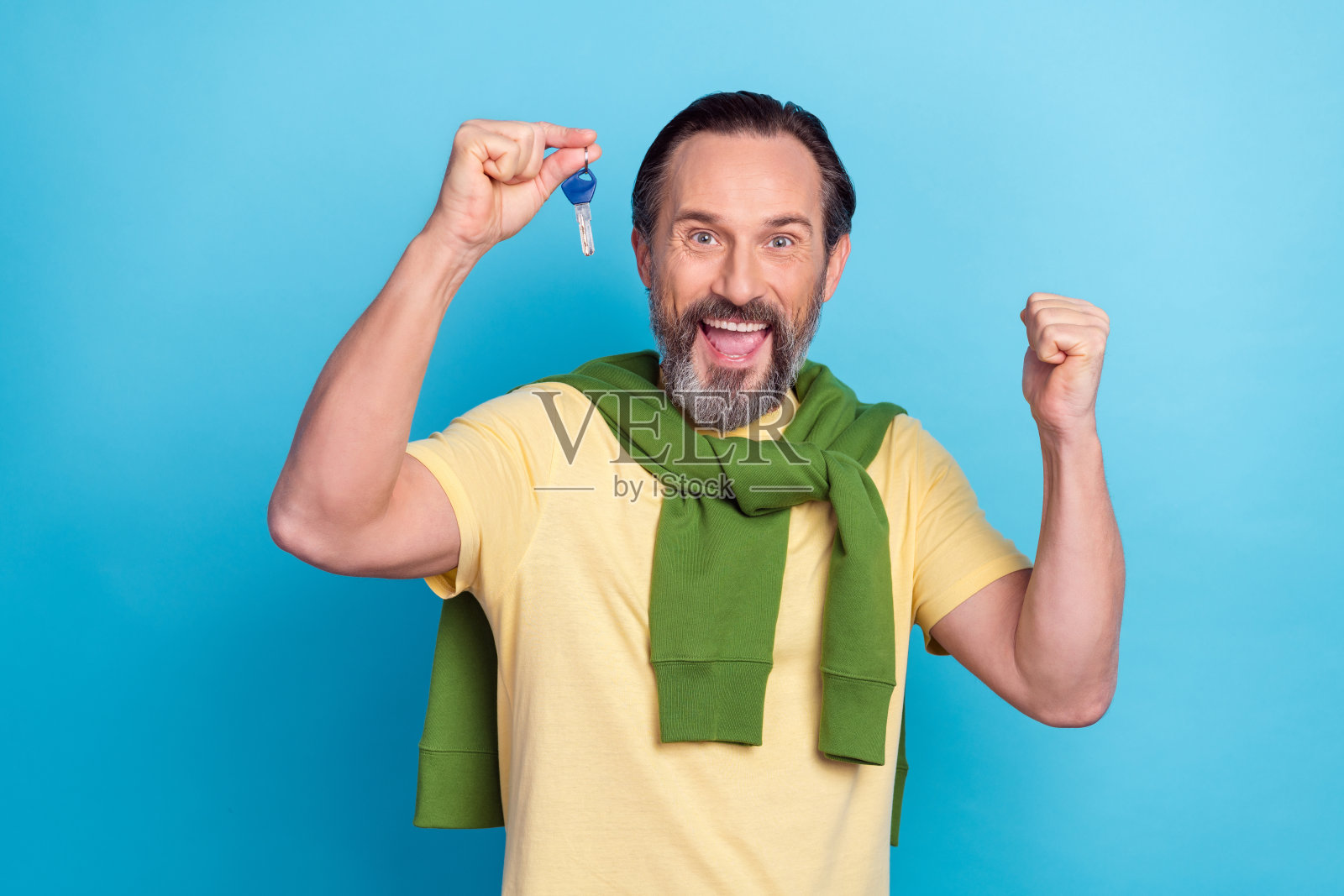 兴奋的幸运帅哥手握钥匙,举拳庆祝,背景为蓝色。照片摄影图片