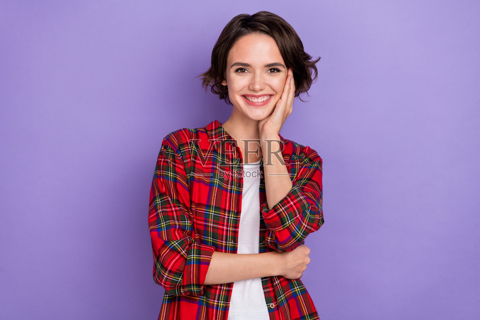 穿着红色衬衫的甜美千禧一代短发女士,手托脸庞,背景为紫色。照片摄影图片