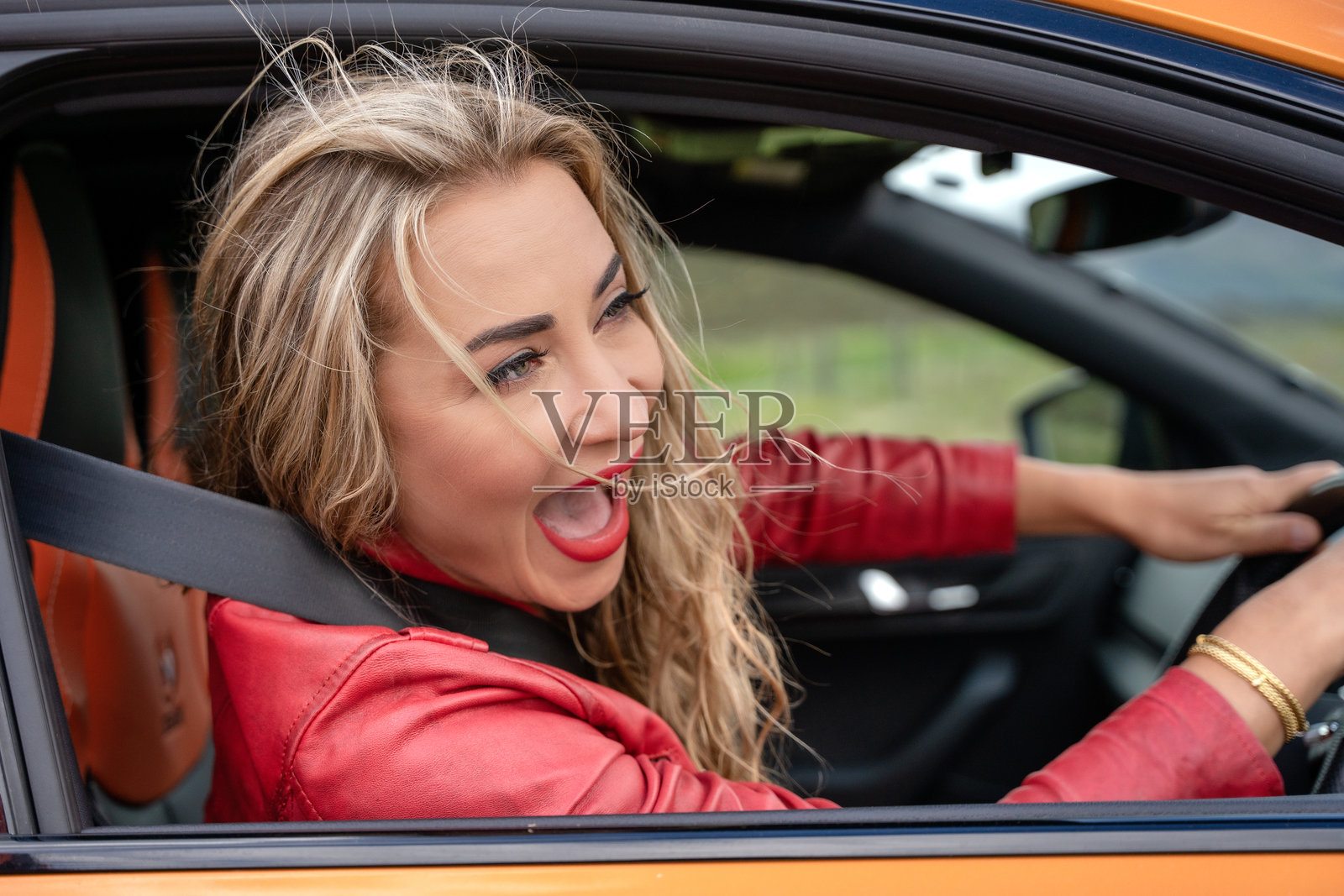 兴奋的女性在乡村阳光明媚的日子里,驾驶着橙色汽车,头发随风飘扬,脸上挂着灿烂的笑容。照片摄影图片