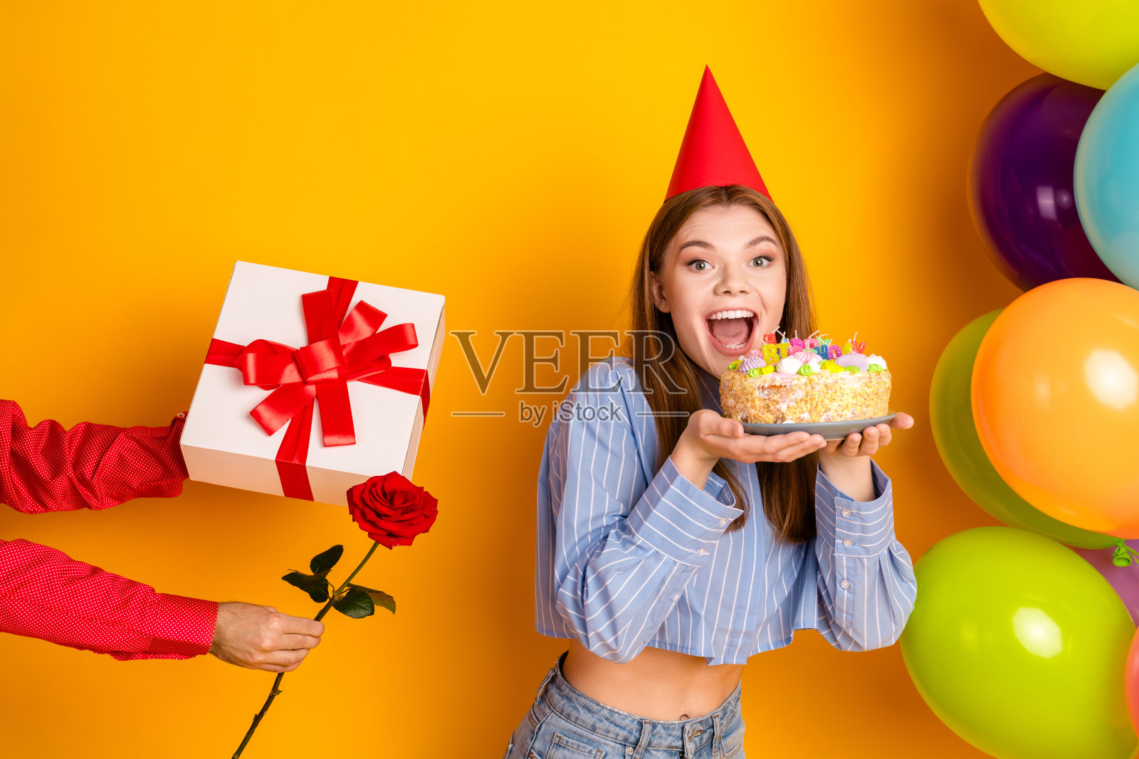 快乐的年轻女性在充满活力的黄色环境中庆祝特别的时刻,周围有气球、蛋糕和礼物。照片摄影图片