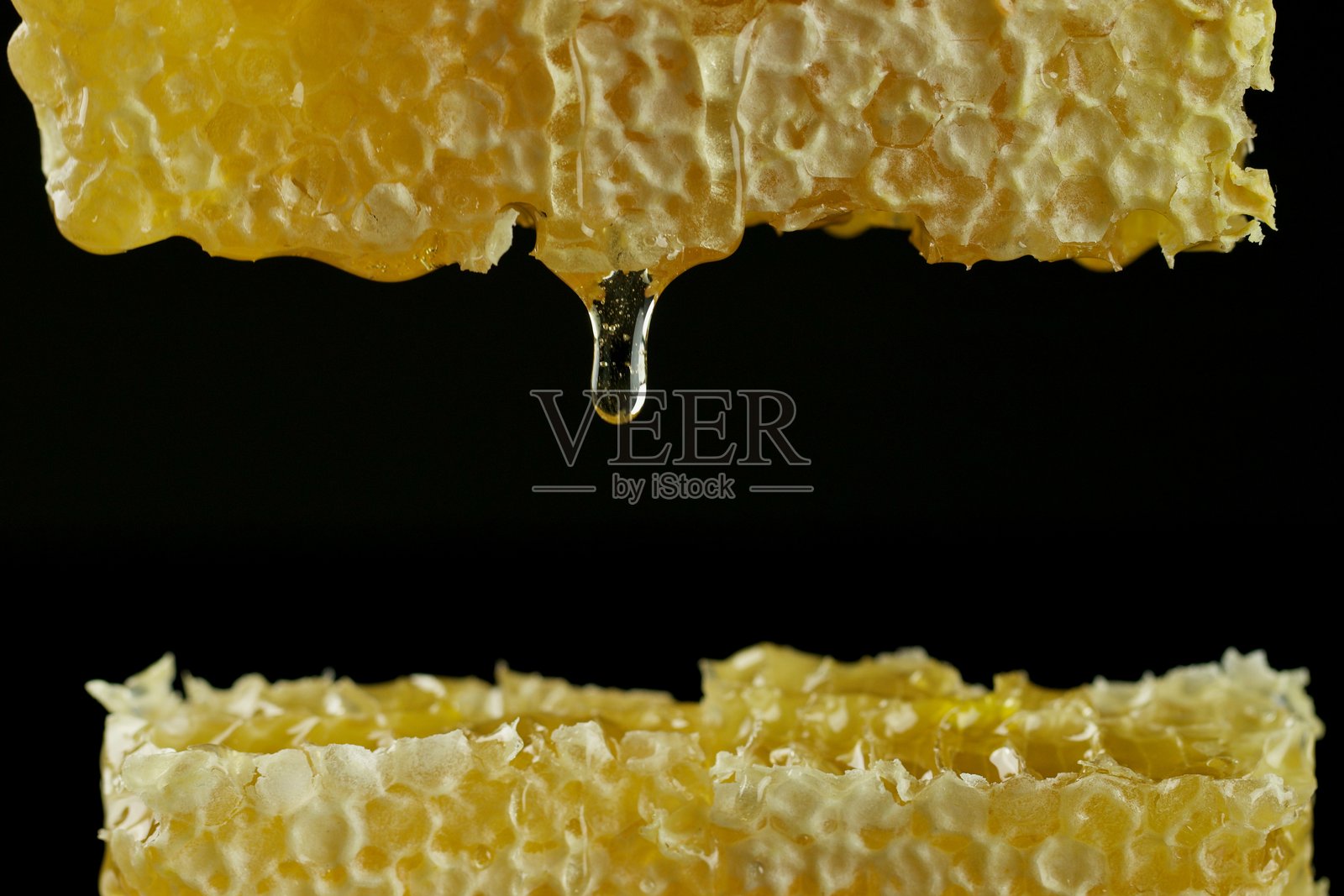 透明的蜂蜜滴从蜂巢流下。特写,深色背景,有文本空间。照片摄影图片
