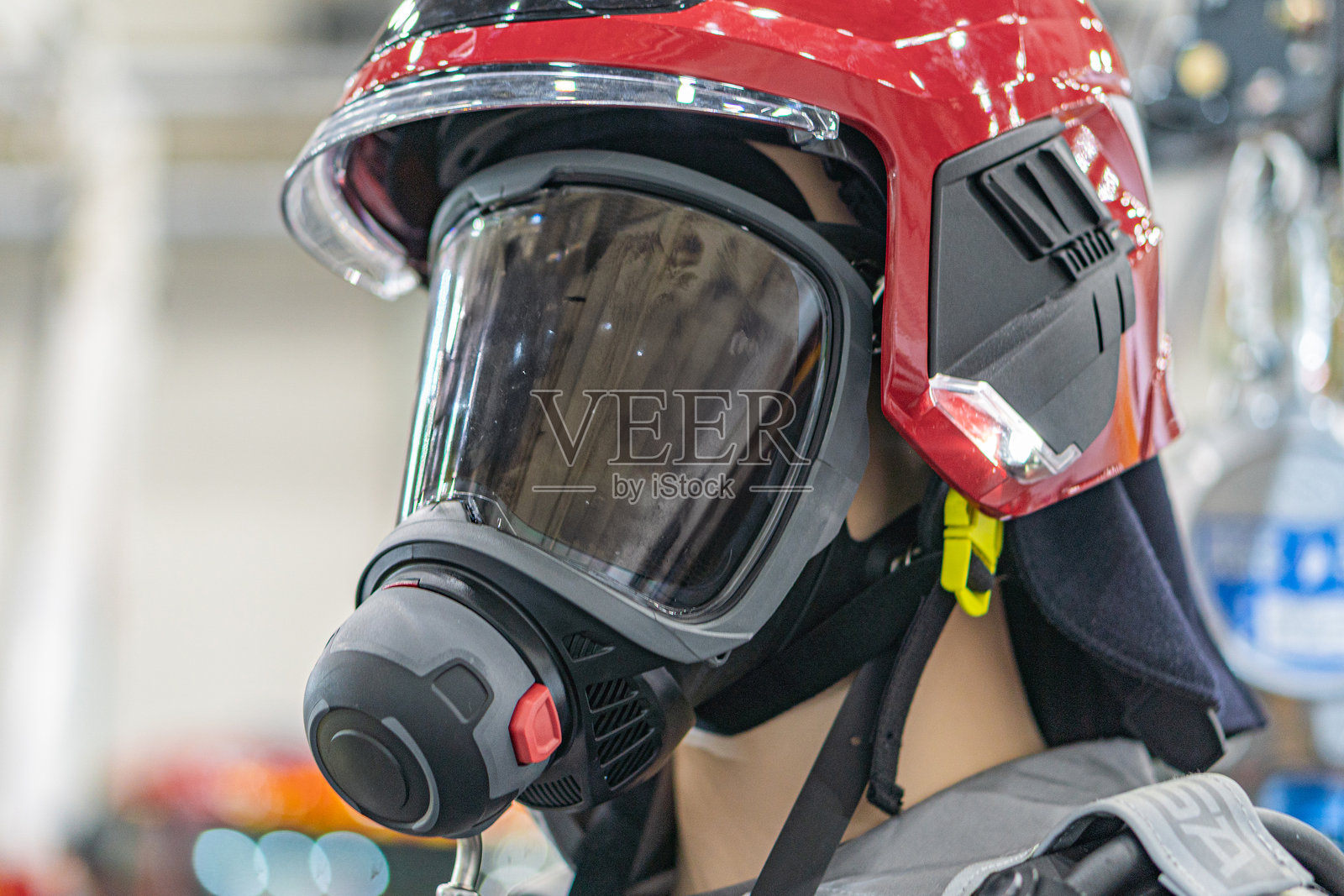 消防员头盔特写,主要为红色,带有黑色装饰,配有附加的面罩和固定带。佩戴者穿着深色阻燃制服。照片摄影图片